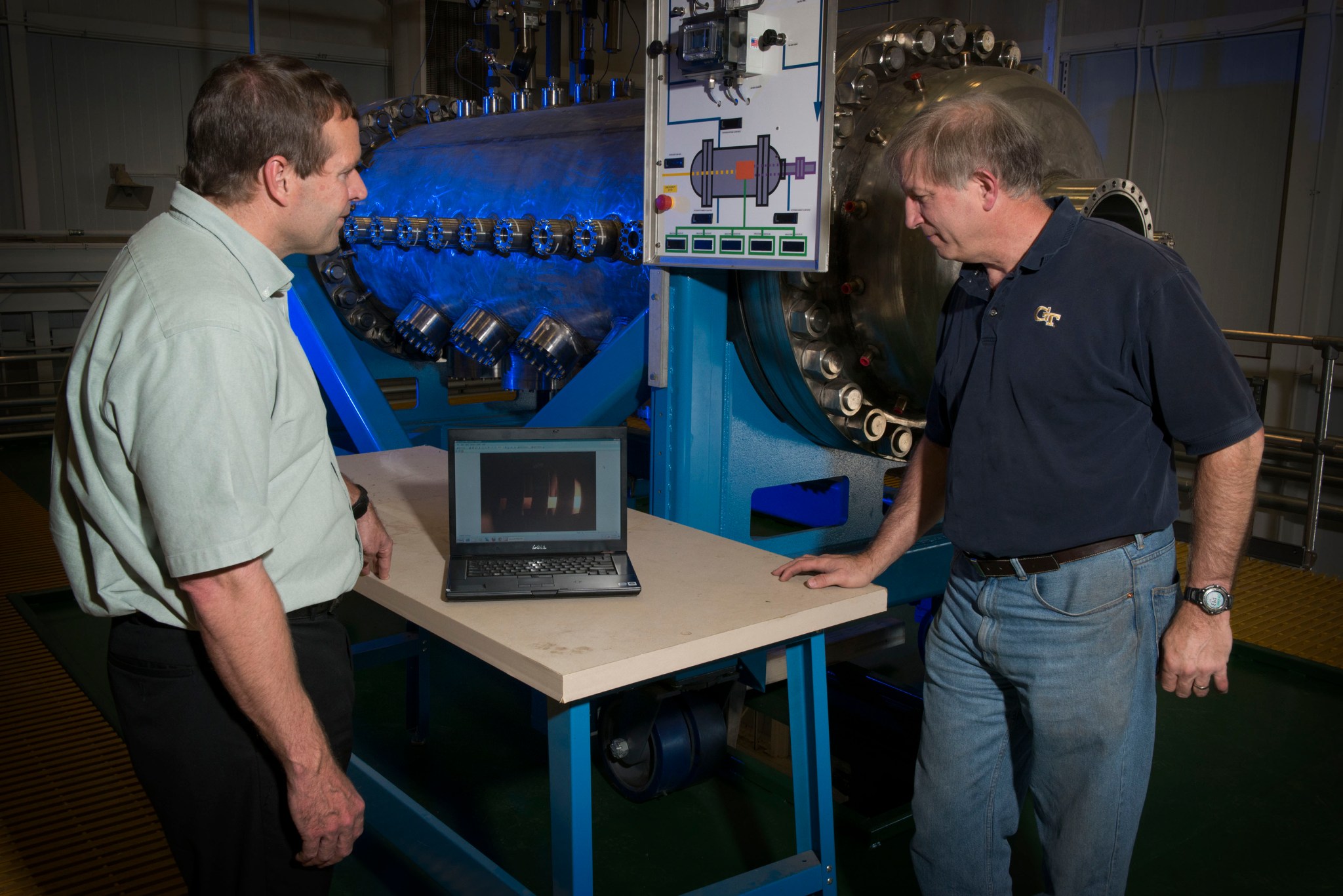 Two men look at a computer on a table in front of Nuclear Thermal Propulsion equipment.