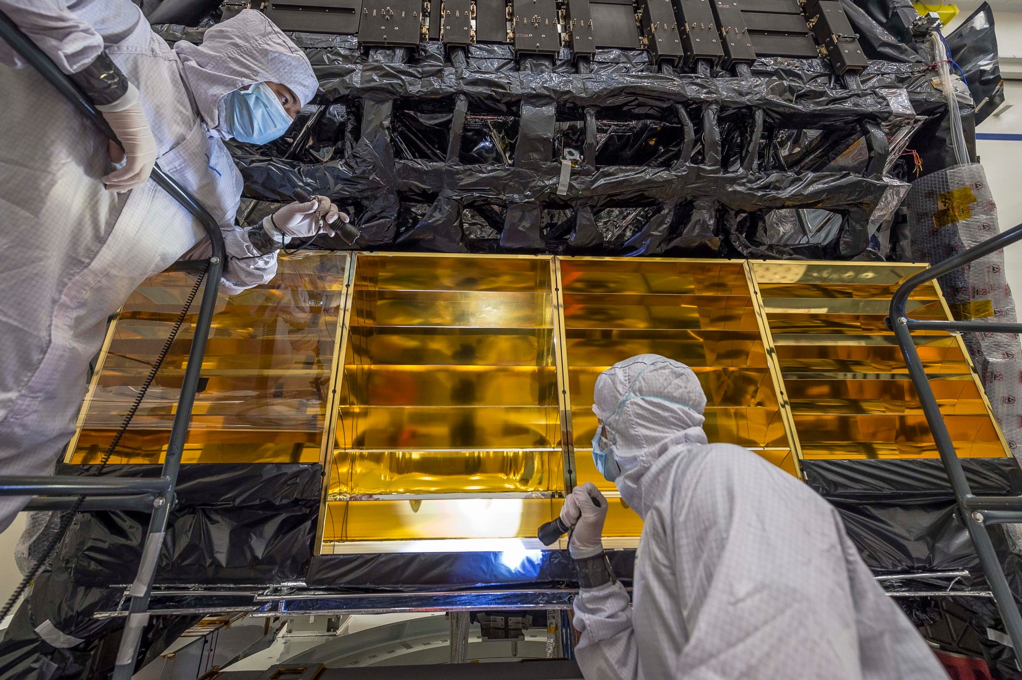 Engineers reinstall one of the gold-plated baffles that helps direct heat away from the integrated science instrument module.