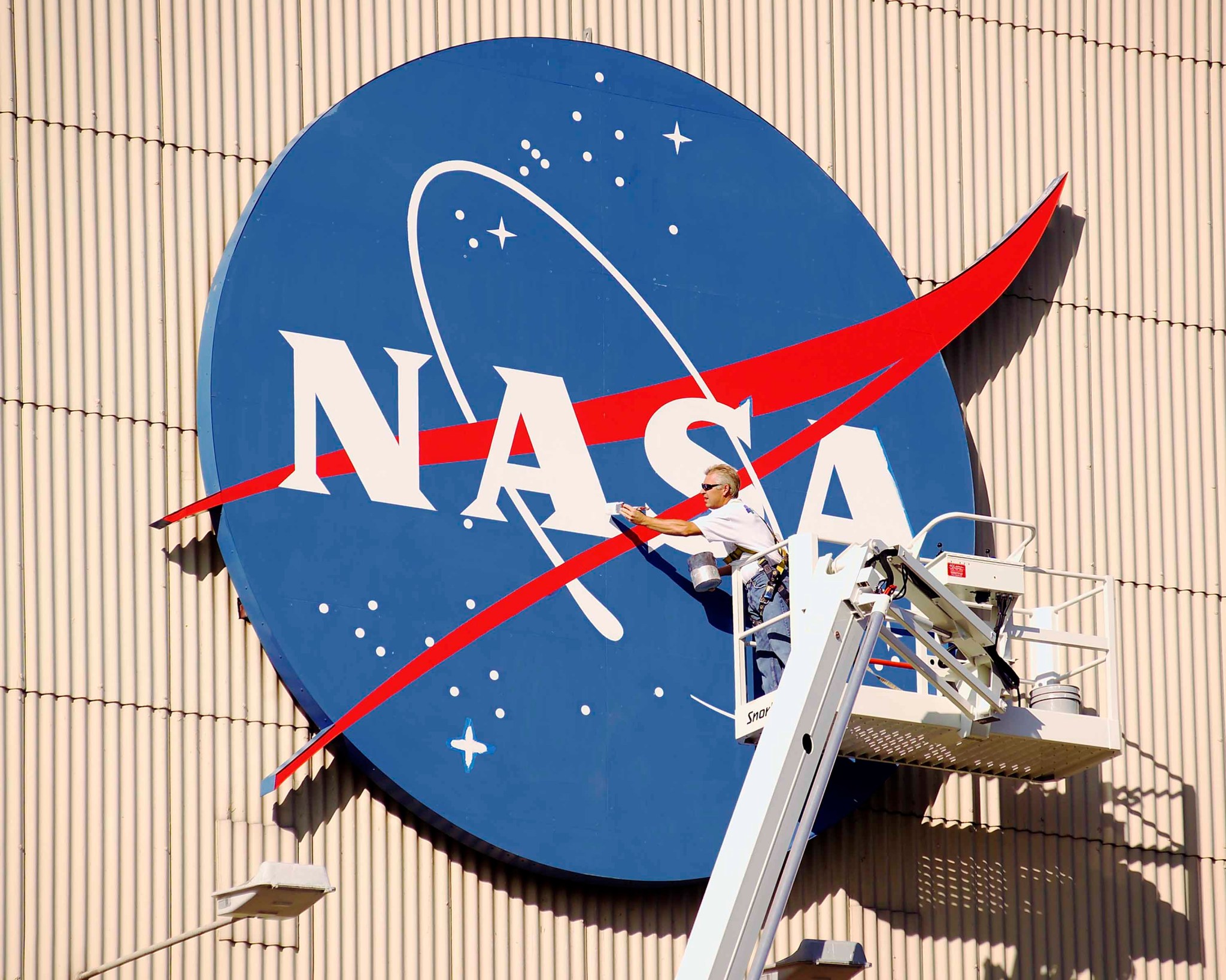 A worker applies fresh paint to the NASA logo.