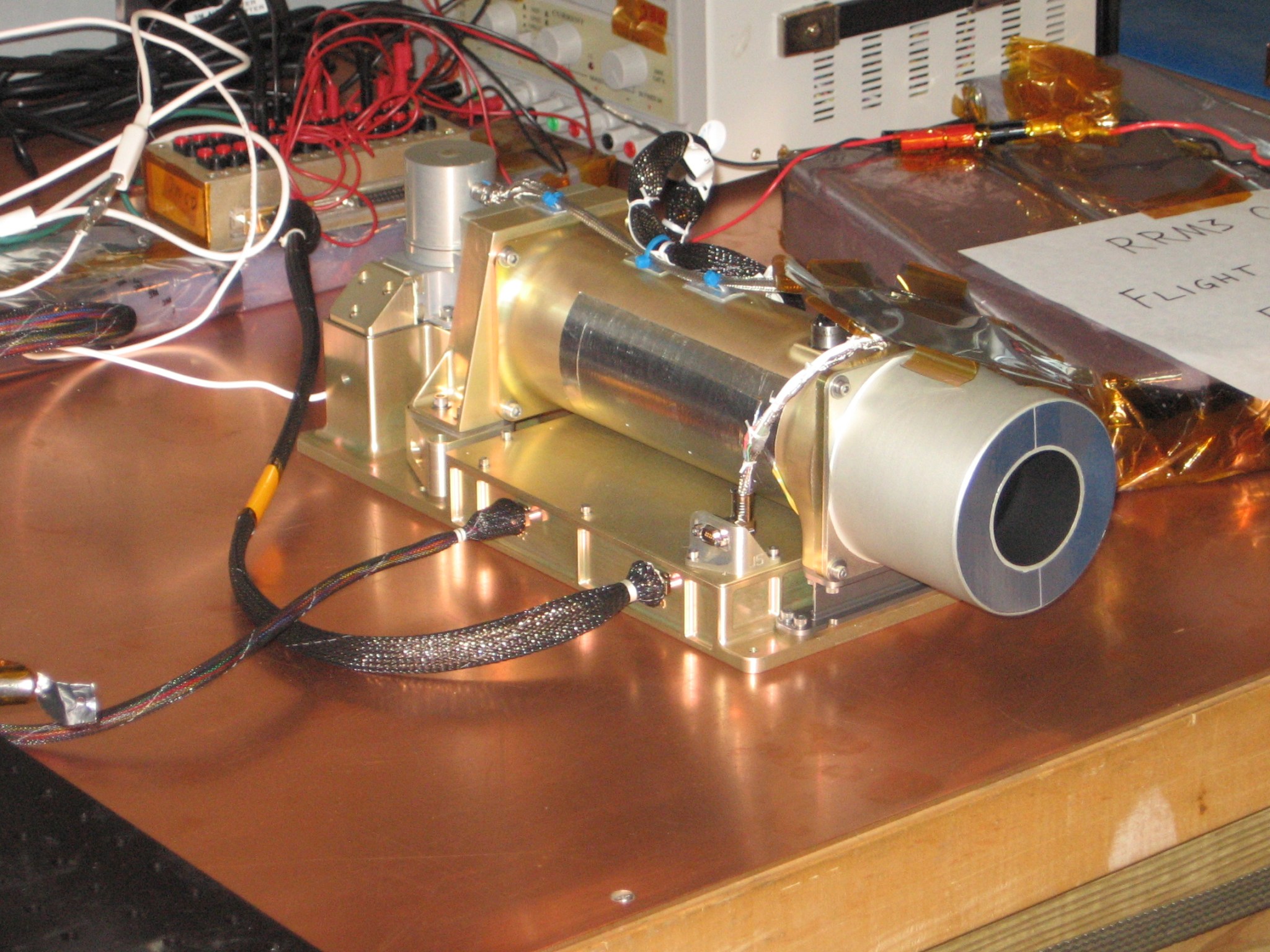 gold cylinder with wires and electrical components on a wooden table.