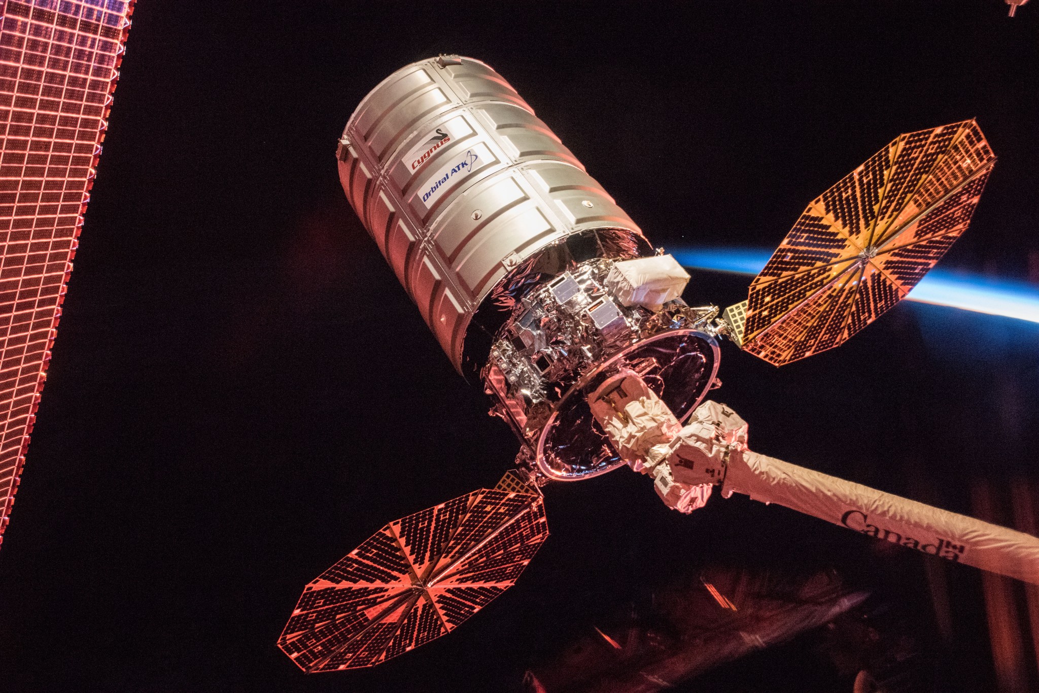 Undocked Cygnus spacecraft at end of robotic arm with solar arrays deployed