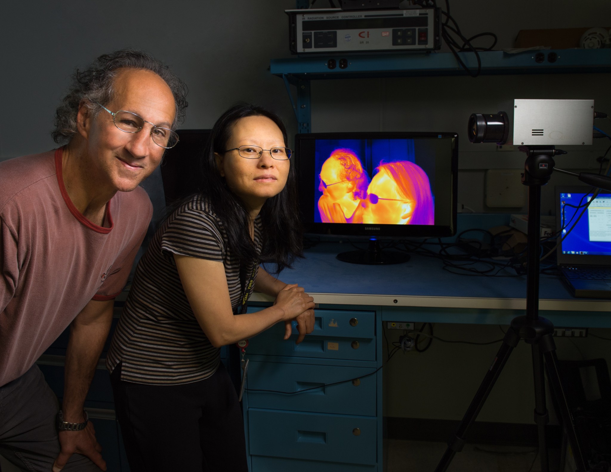 man with curly grey hair and woman with straight black hair stand in front of a monitor showing them in infrared.