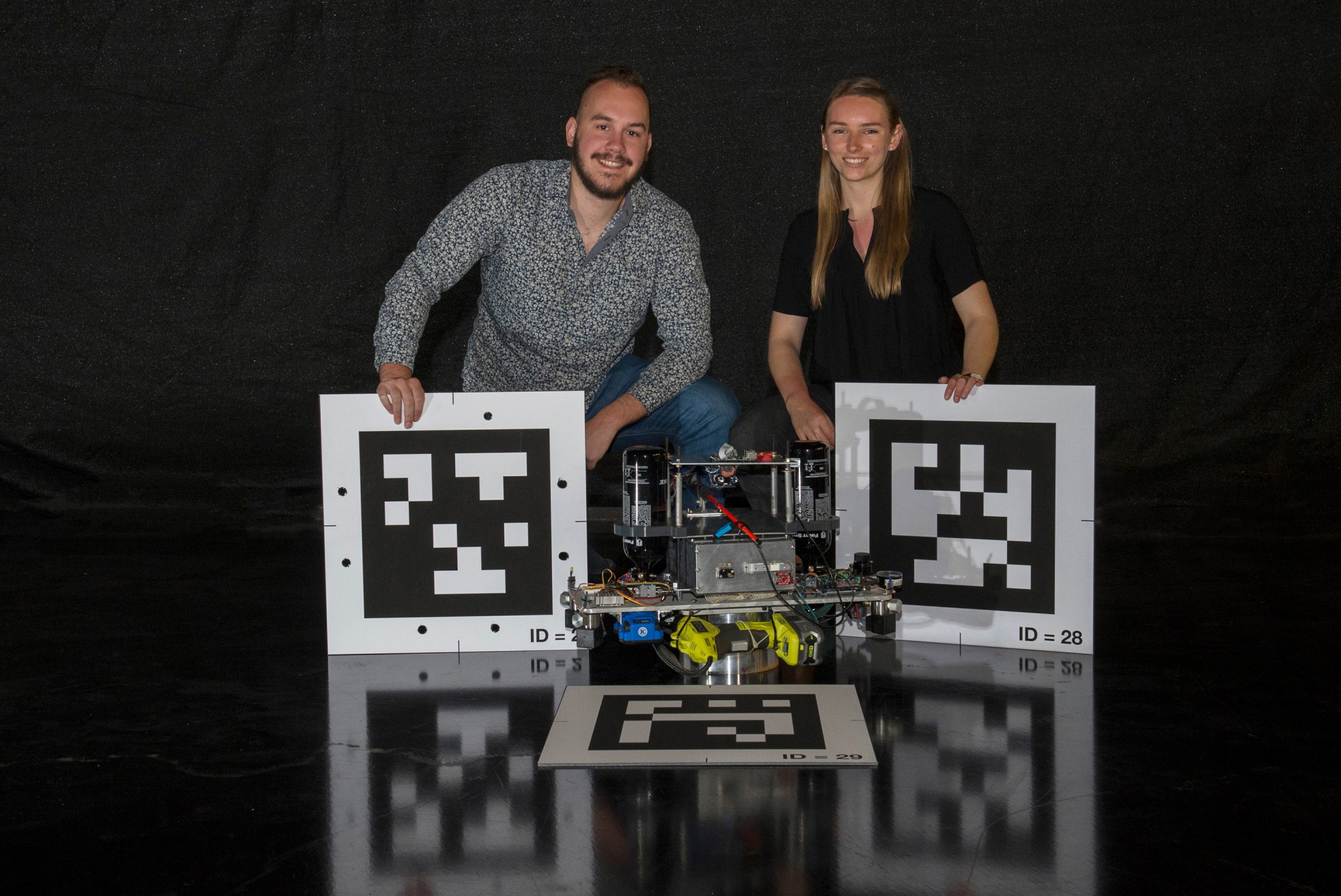Engineering interns Tristan Schuler, left, and Greta Studier pose with 2D barcodes and a Nano Air-Bearing Simulator prototype.