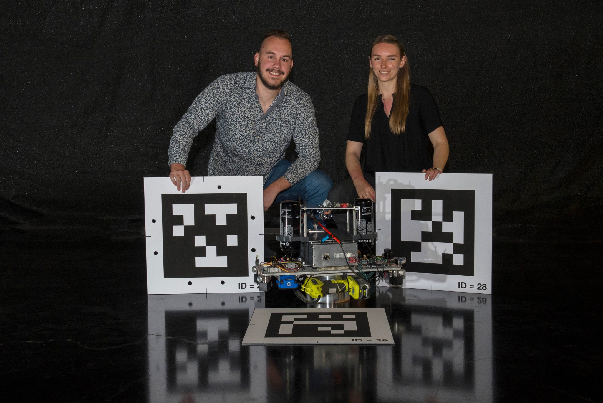 Engineering interns Tristan Schuler, left, and Greta Studier pose with 2D barcodes and a Nano Air-Bearing Simulator prototype.