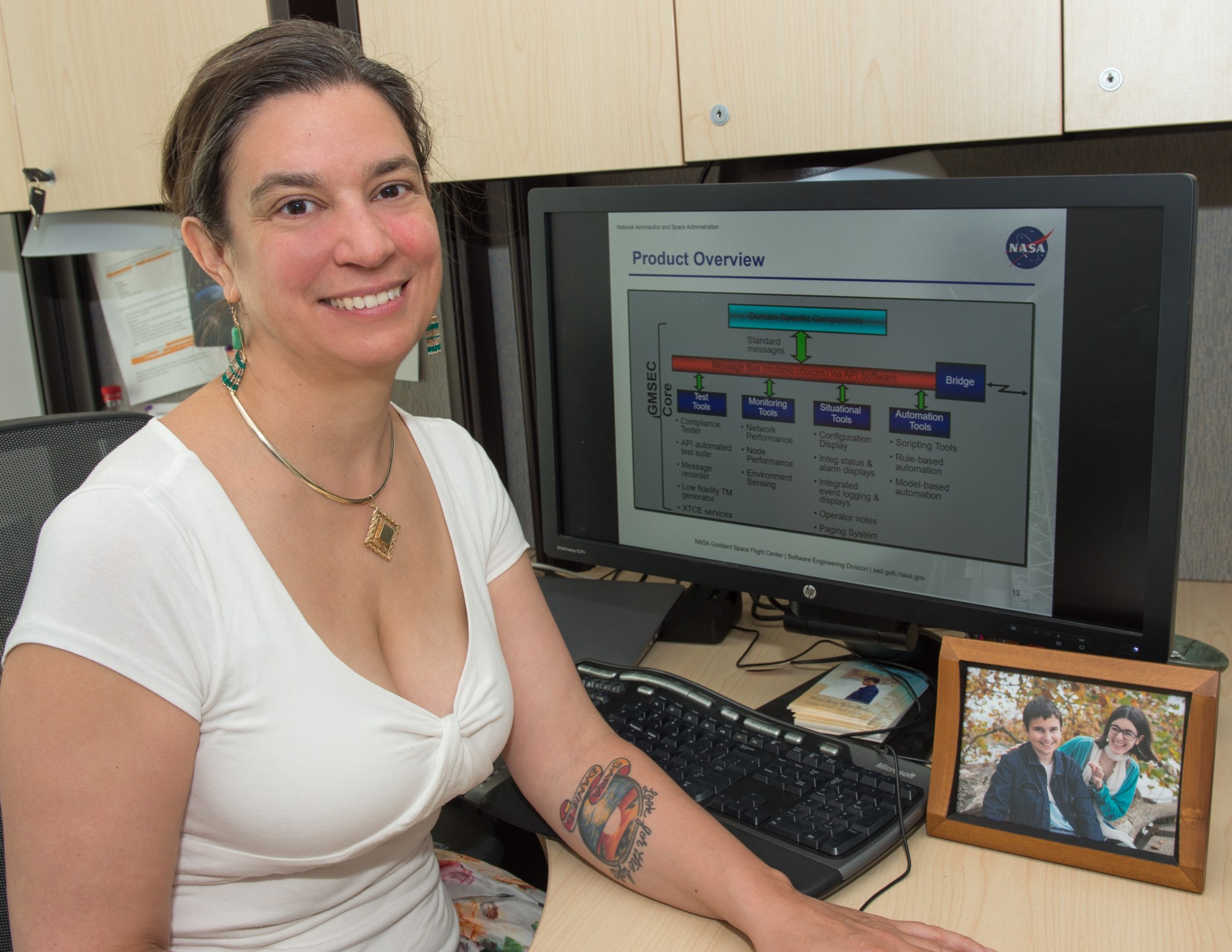 Woman with brown hair, wearing a white top , in her office, a picture of her and her son on her desk.