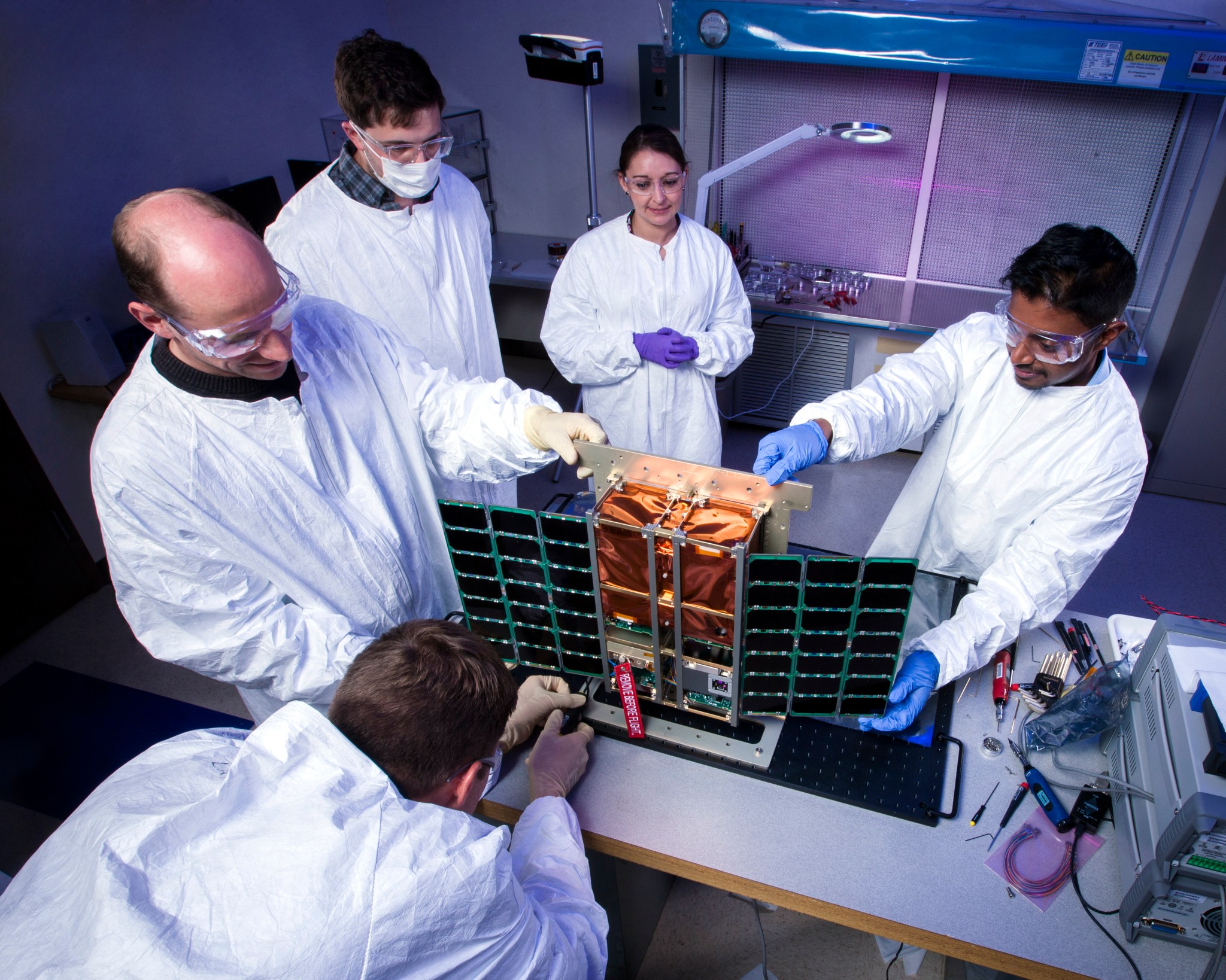 Five people in white lab coats standing around an instrument with a copper colored center and panels on either side.