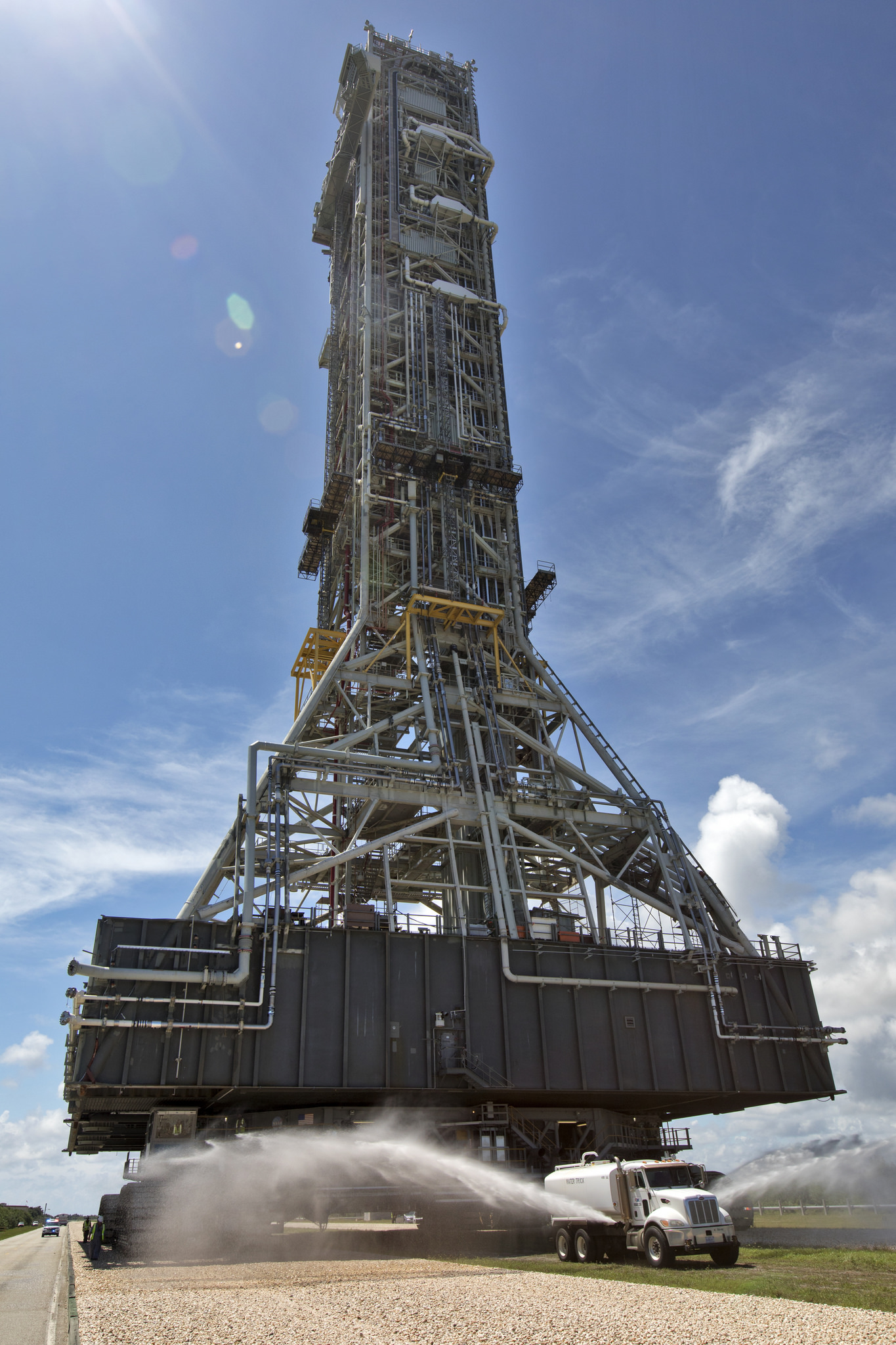 A truck sprays water in front of the mobile launcher atop crawler-transporter 2 as it moves toward Launch Pad 39B at KSC.