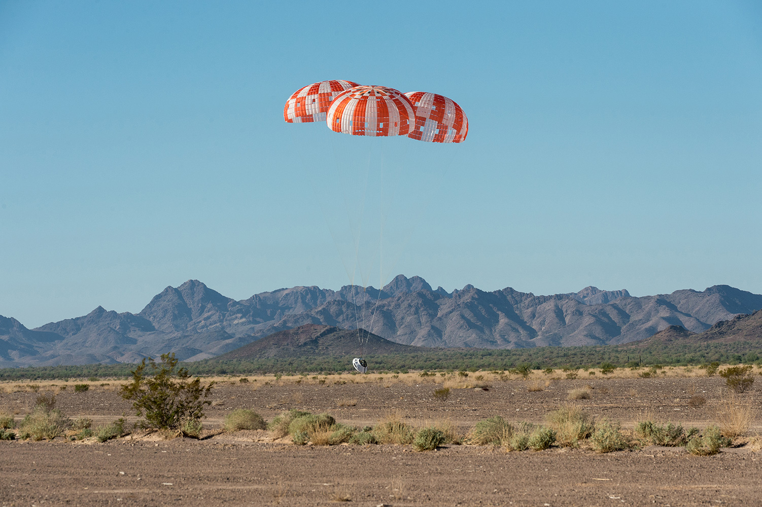 An Orion test capsule with its three main parachutes