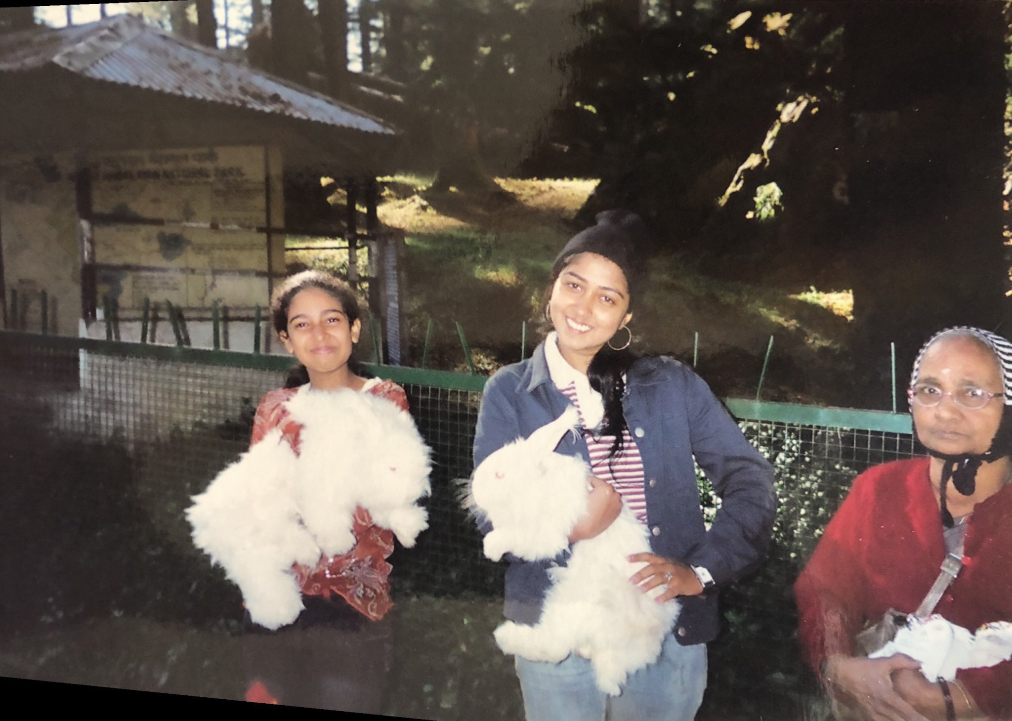 Older photo of three women, two young women and one older, the two younger women giant angora rabbits bred for their wool.