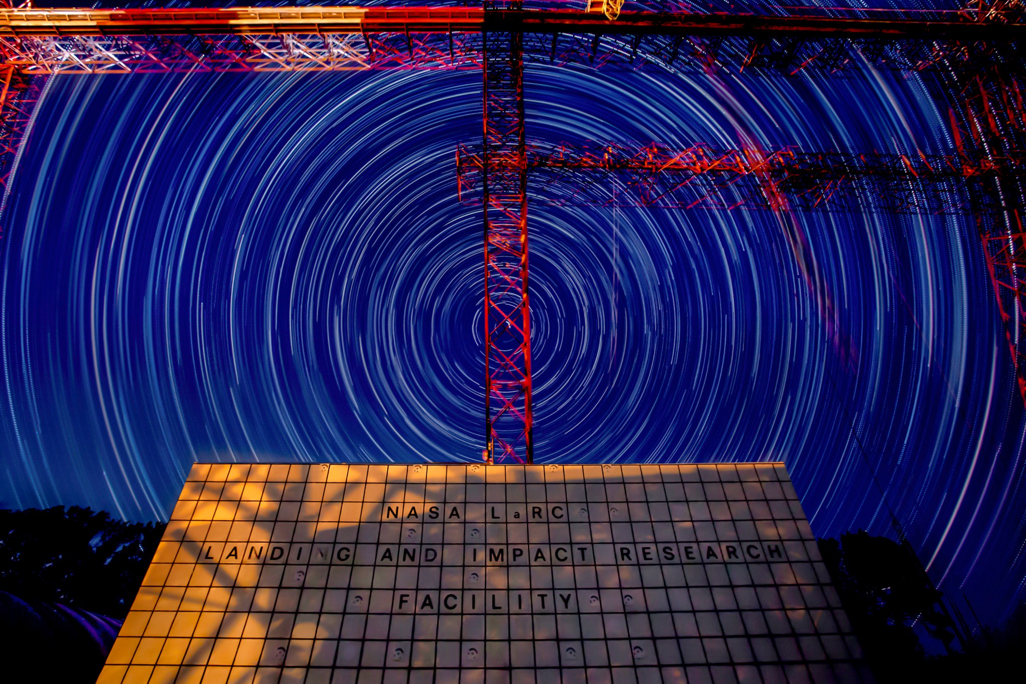 This is a time-lapse still photograph of night time over the gantry at NASA Langley Research Center. Stars appear to swirl in a circle over the gantry against the dark blue night sky.