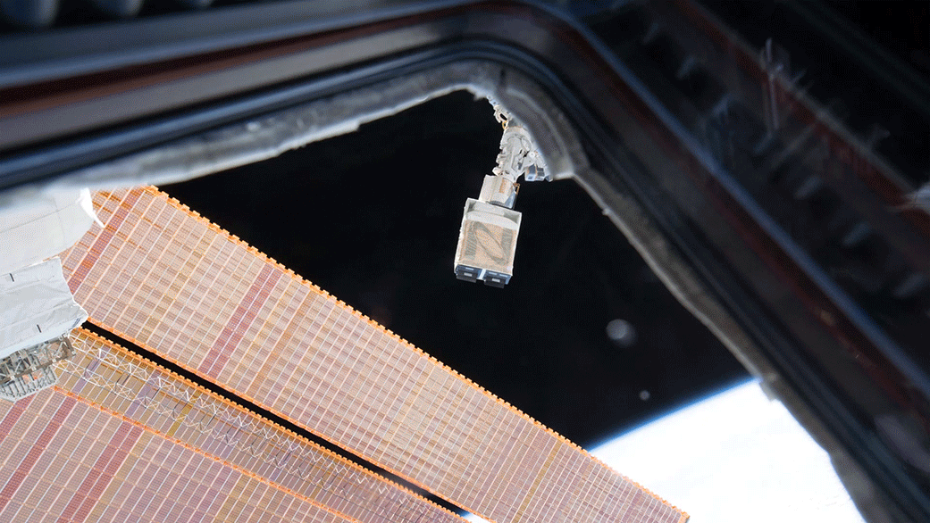 Dellingr CubeSat deployment video. showing a little dark rectangular box-shaped satellite shooting out of a white instrument on the Space Station. Dellingr floats between the camera and two long, gold solar panels before floating in front of the blue and white limb of Earth seen from space,