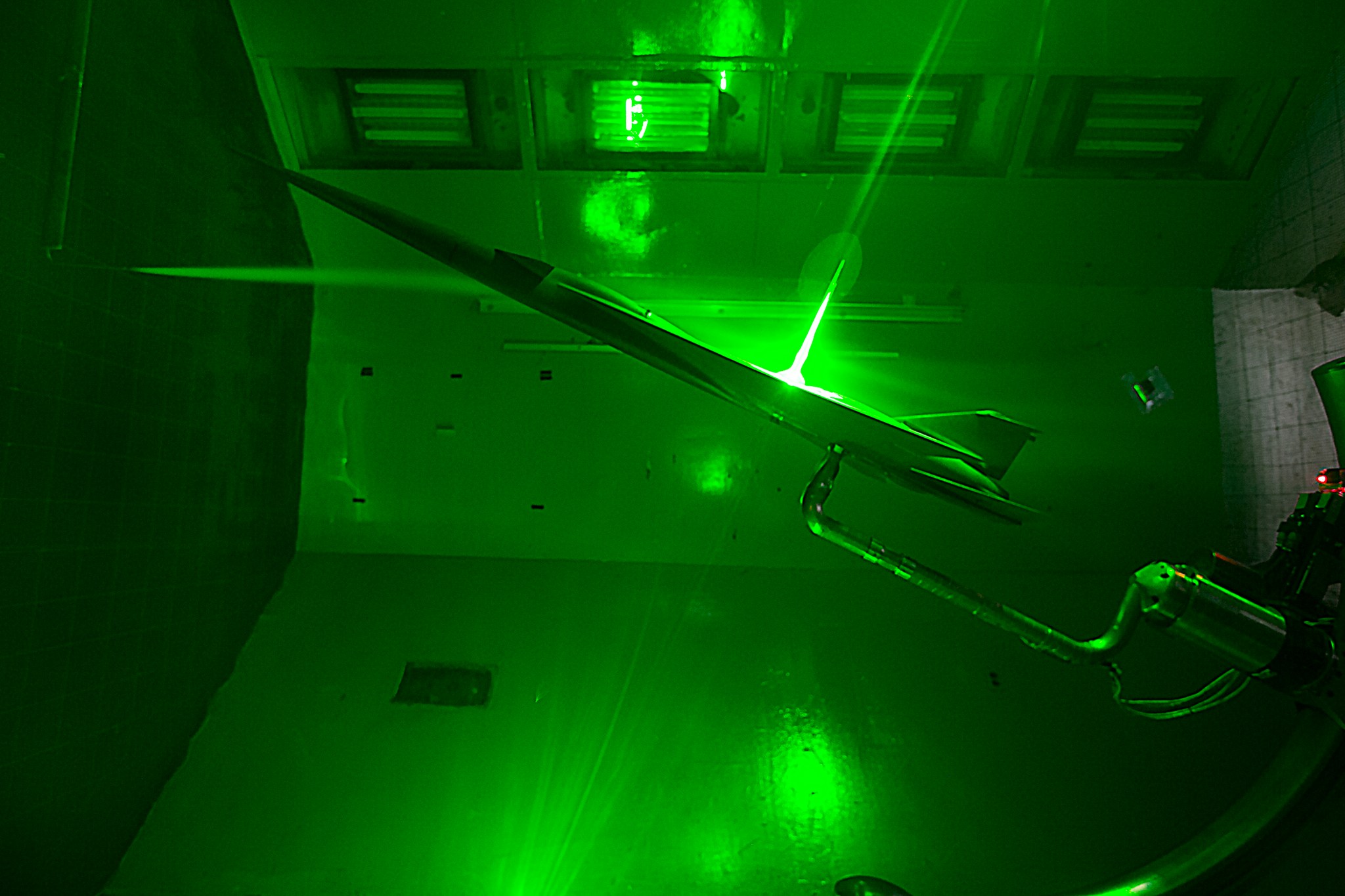 A sub-scale X-59 model undergoes testing in the 12-Foot Low-Speed wind tunnel using smoke and lasers to gather data.