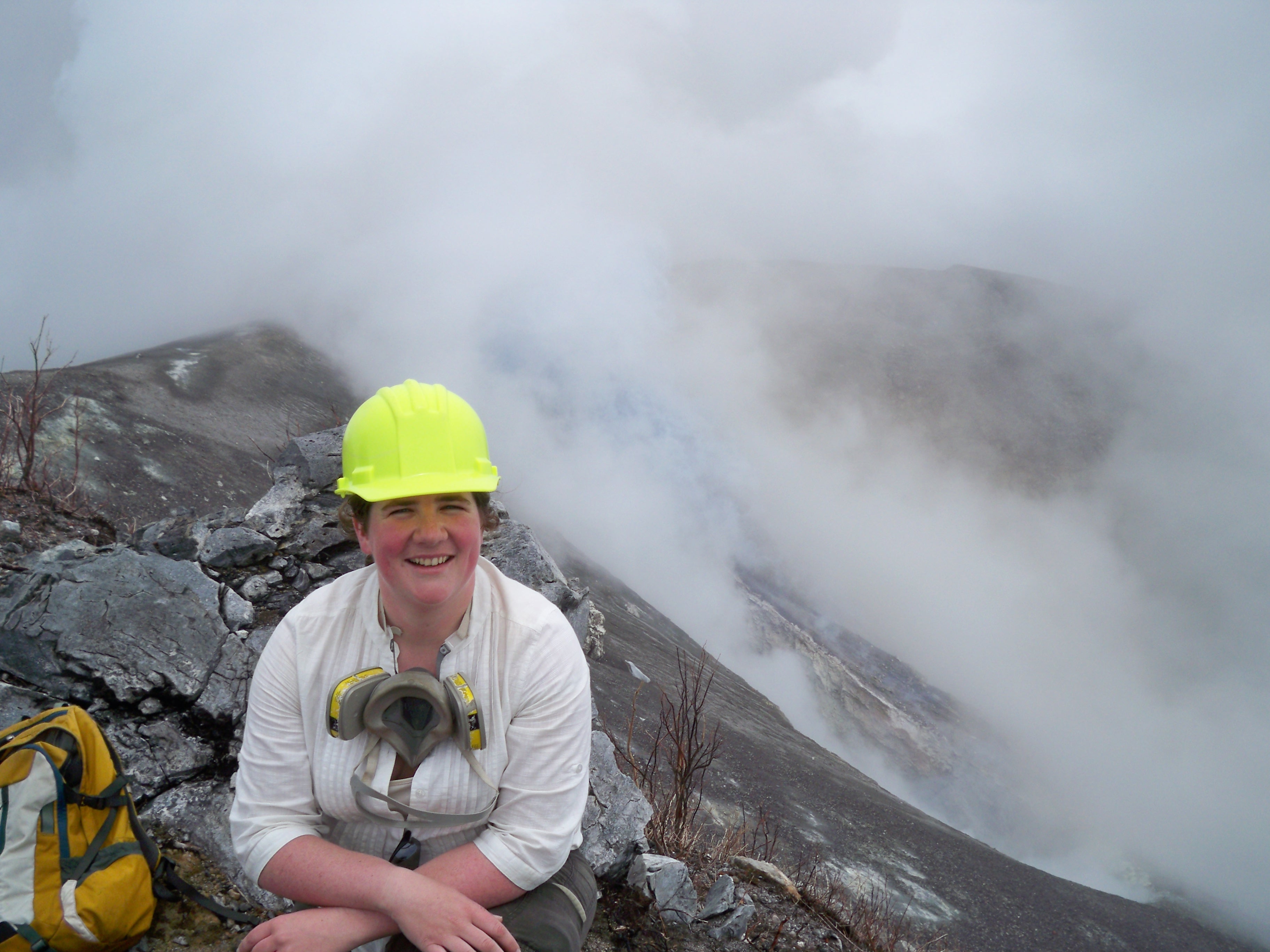 Woman wearing a white shirt and yellow hard hat sits near a volcano vent on the Turrialba volcano