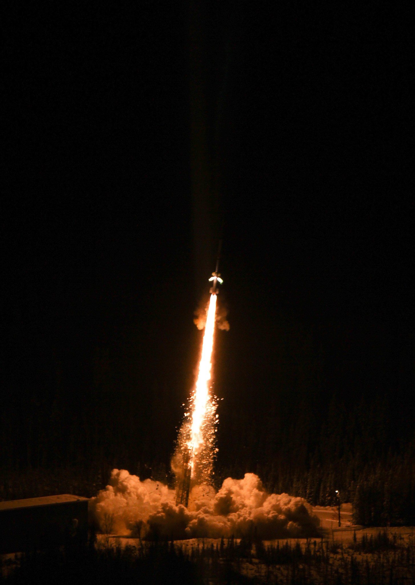 An image of a sounding rocket launching at night, the rocket just visible over a stream and cloud of bright orange flame.