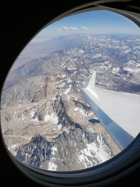 An aerial view of the Sierra Nevada mountain range out an airplane window with the wing visible..