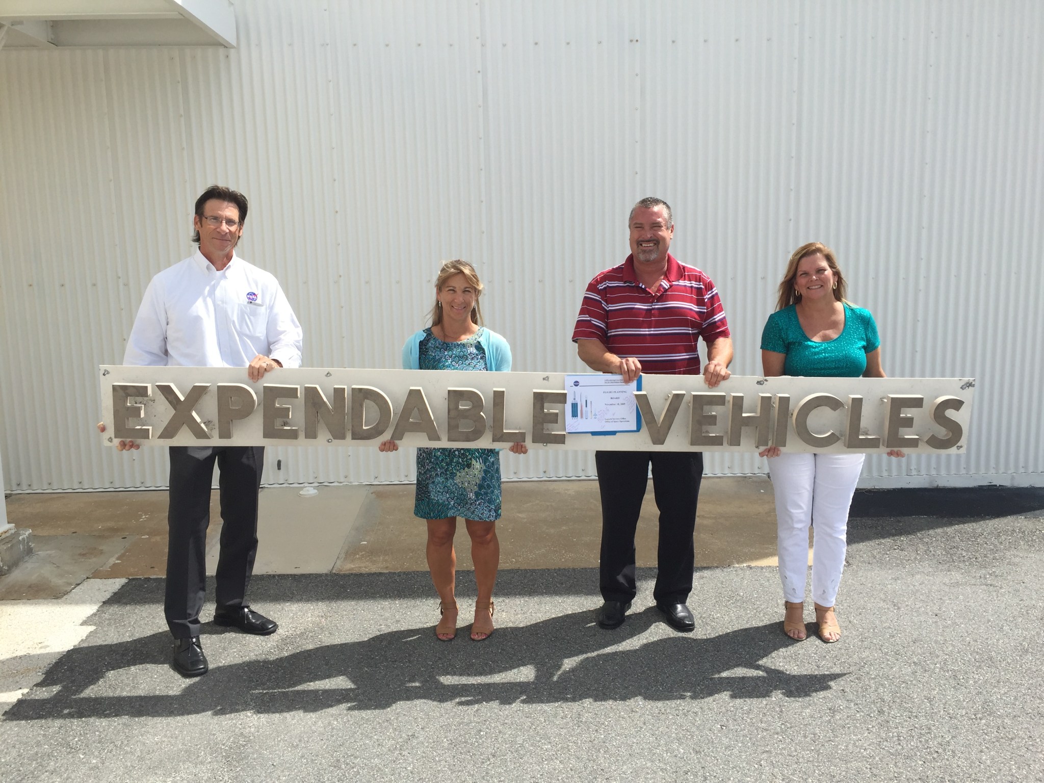 Four LSP team members hold the retired Expendable Vehicles sign at the E&O Building at CCAFS.
