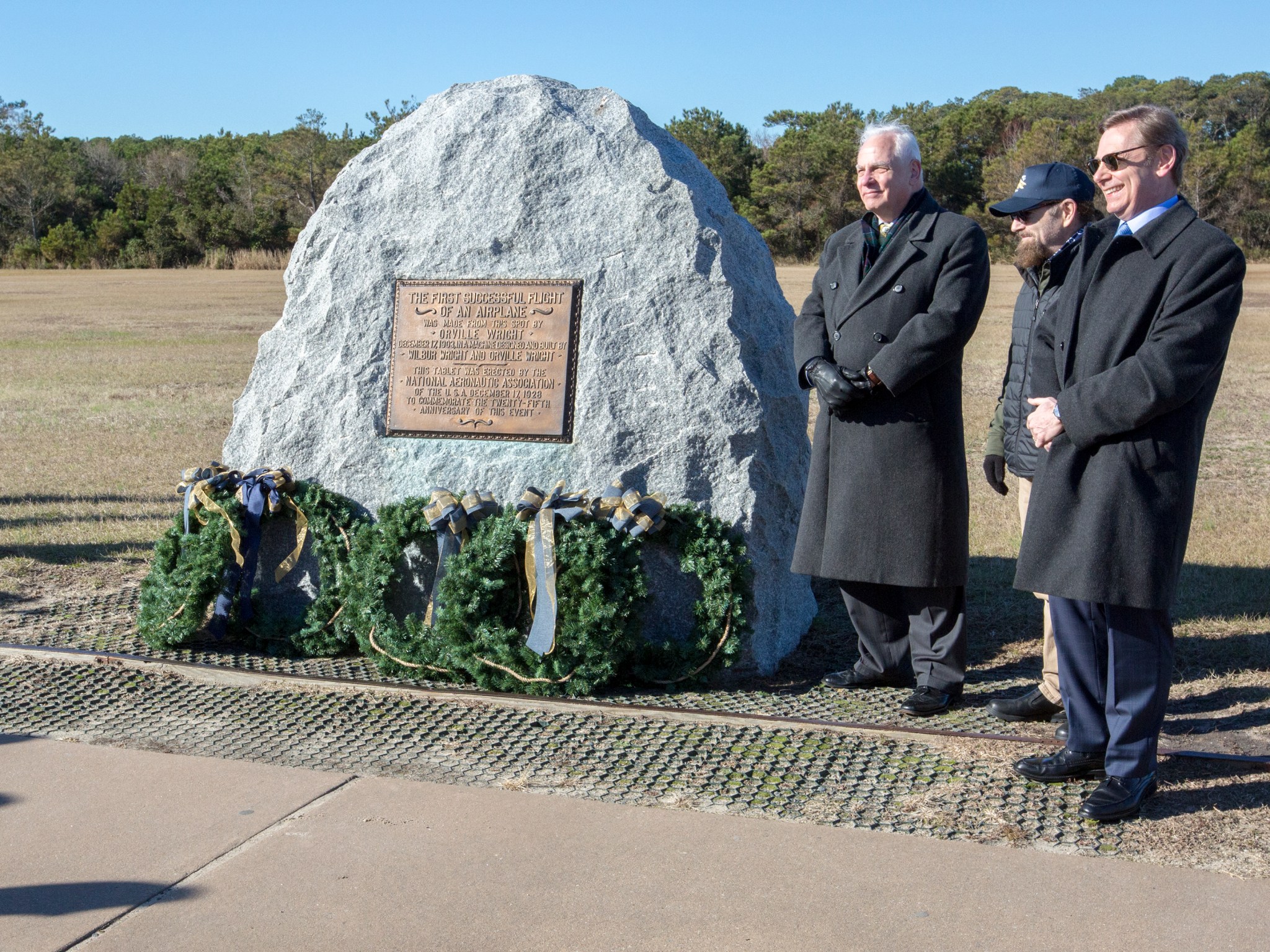 Descendants of the Wright Brothers' family stand next to a marker adorned with wreaths honoring the Wright Brothers.