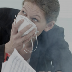 Woman holding a respirator to her face in a smoky environment