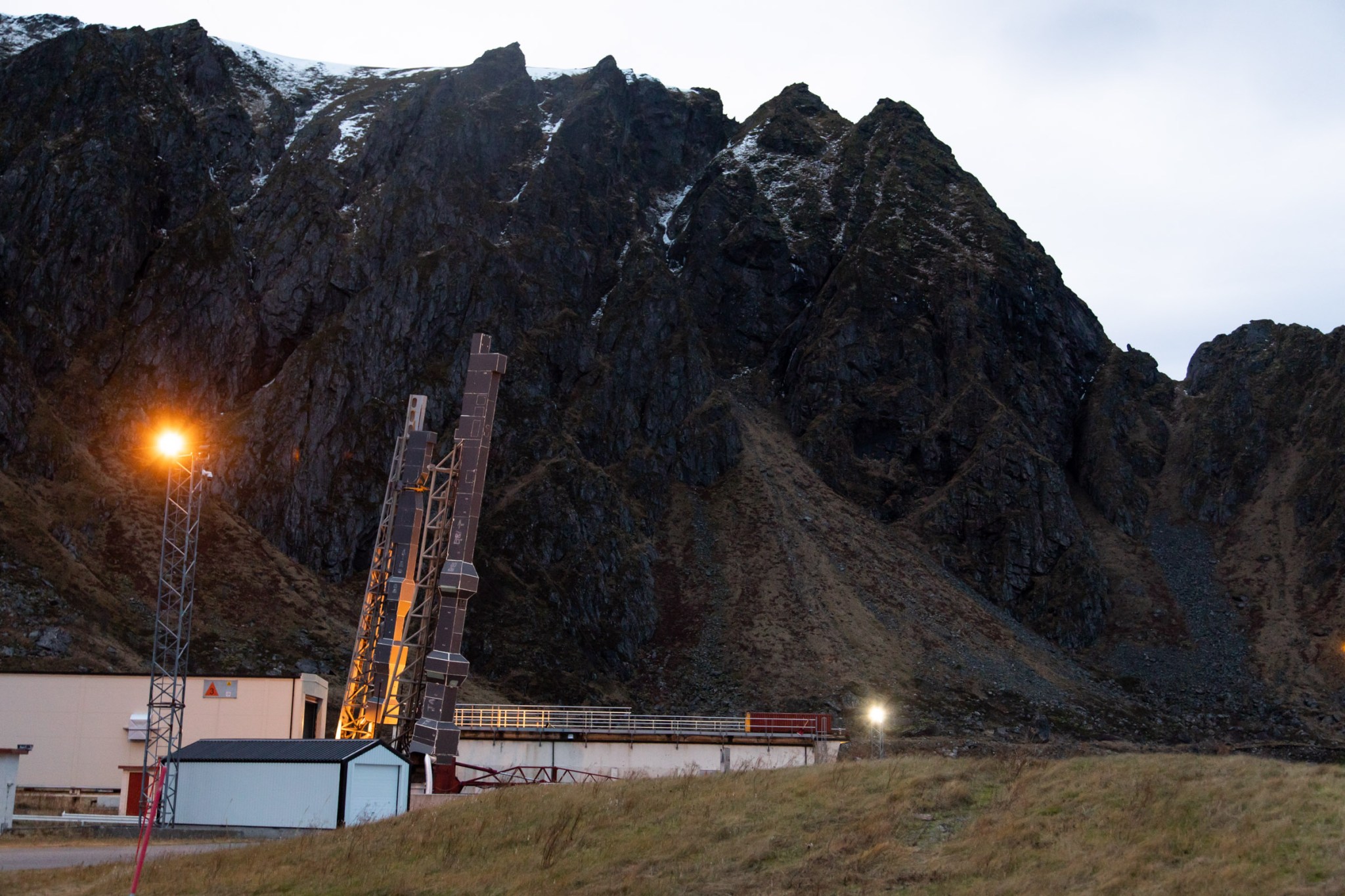 TRICE-2 rockets in launch position for dress rehearsal 2 Dec 2018. The rockets are held up by scaffolding at an angle slightly off 90 degrees from the ground. Behind the rockets, a jagged mountain range rises against a bright blue sky.