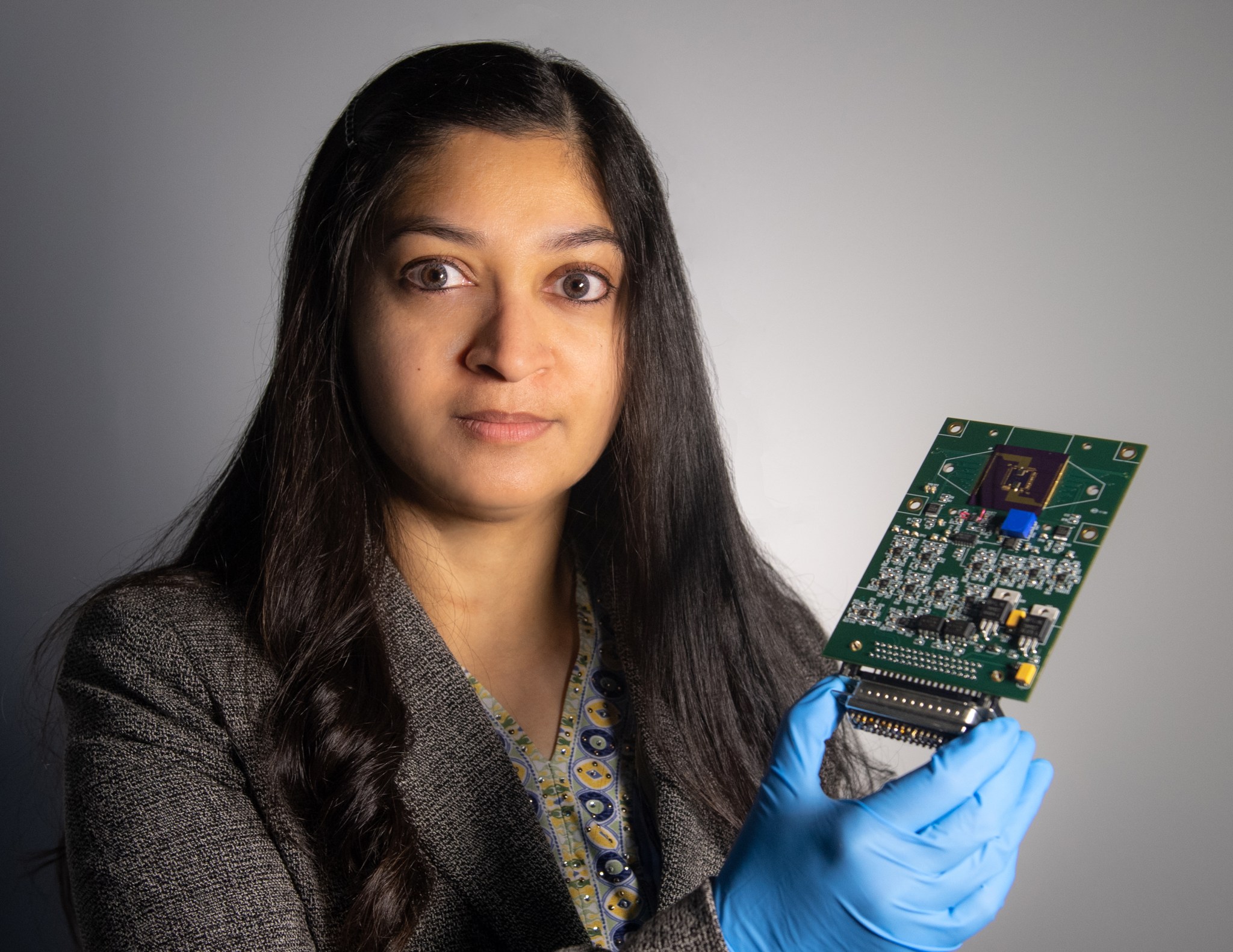 Technologist Mahmooda Sultana, woman with tan skin and black hair holds a sensor platform with several computer microchips