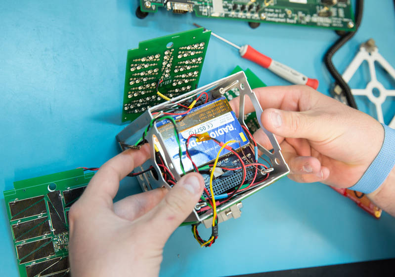Two hands holding a tiny cubesat component, which is open to show wires and electrical equipment.