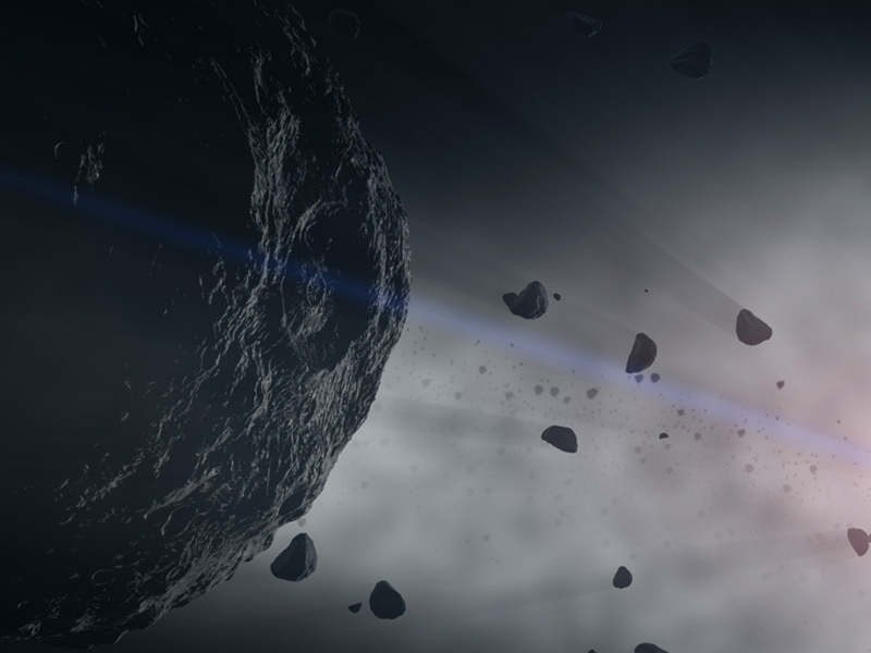 An illustration shows a round, dark-gray asteroid filling the left half of the frame with small, irregularly shaped asteroid fragments scattered near it on the right side.