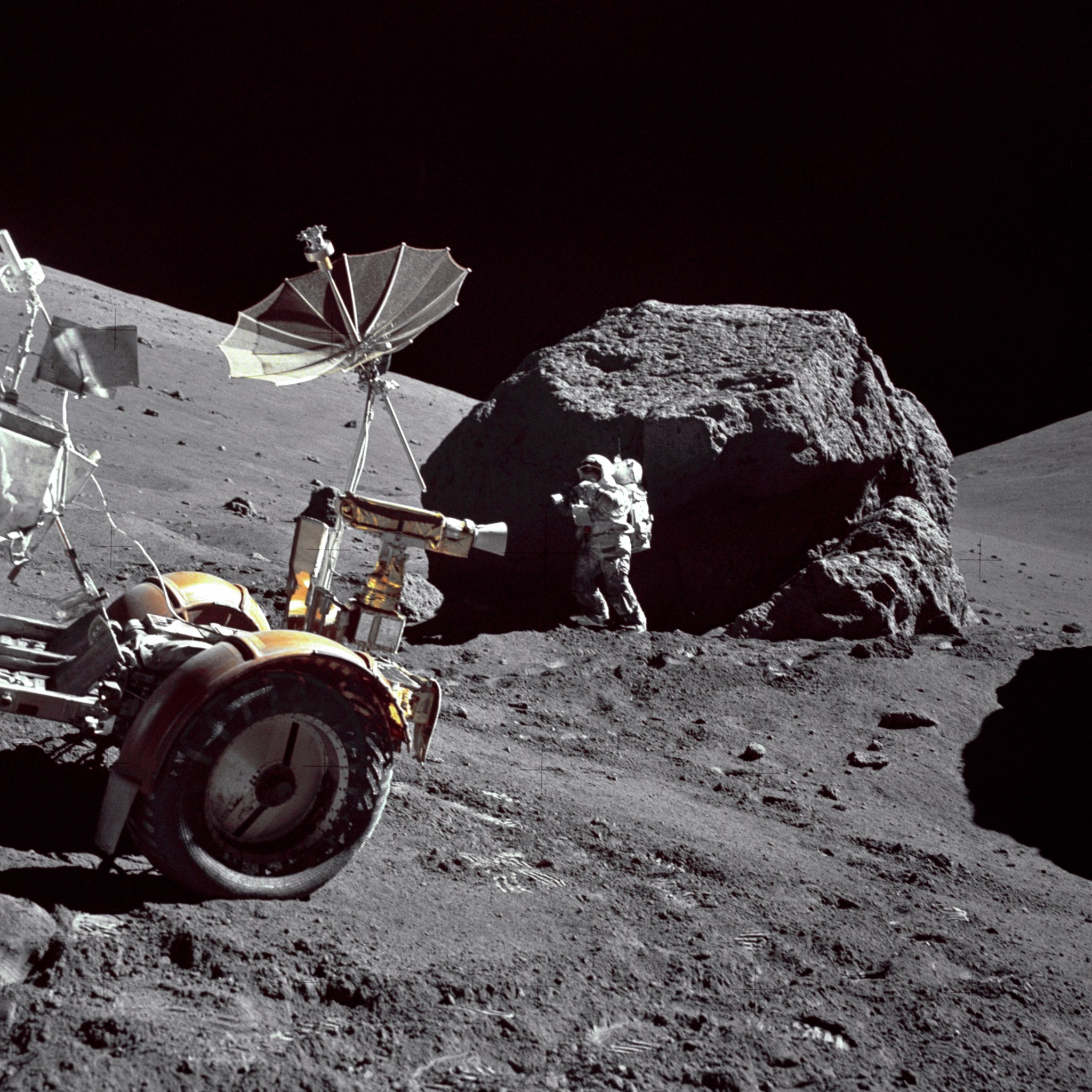 Astronaut on the Moon next to a bolder, with a rover in the foreground.