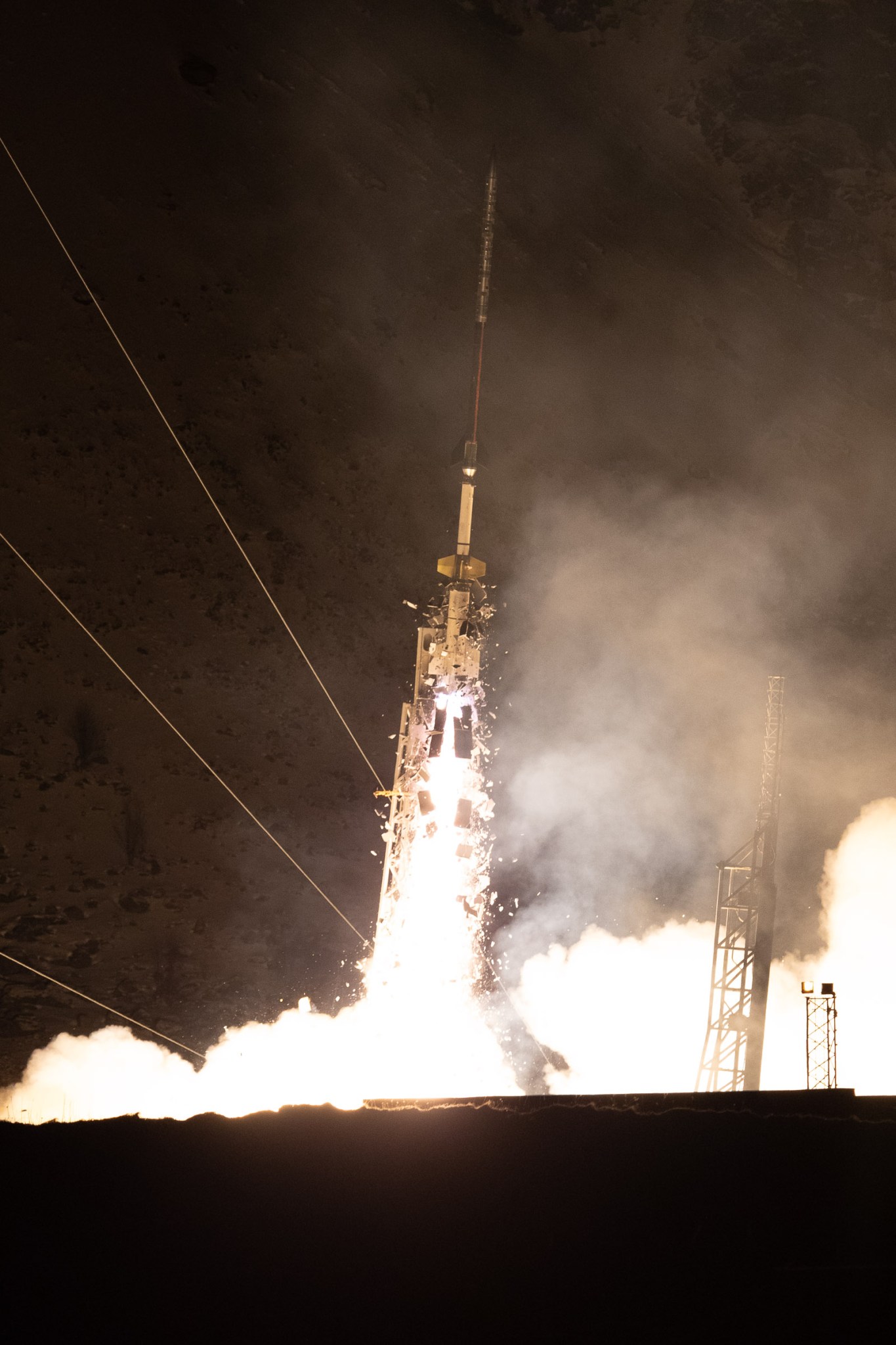 AZURE liftoff. A thin rocket launches in the dark. The rocket fire lights up clouds of white exhaust surrounding the bottom of the rocket.