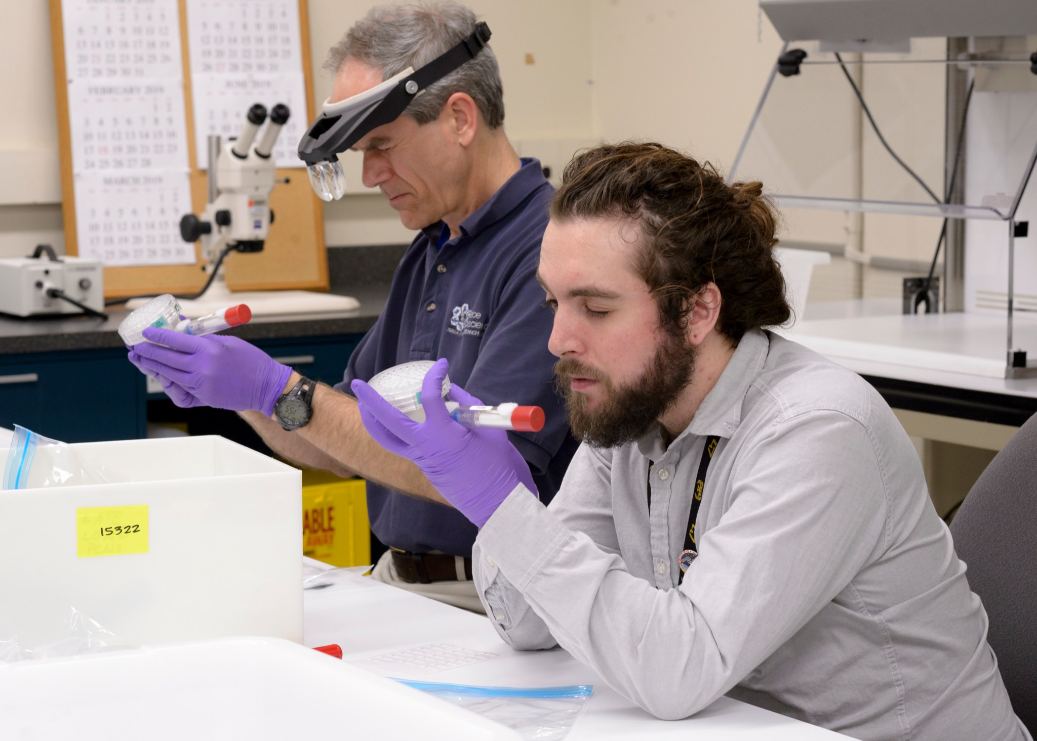 Two men hold experiment hardware, squinting as they precisely apply tiny labels.