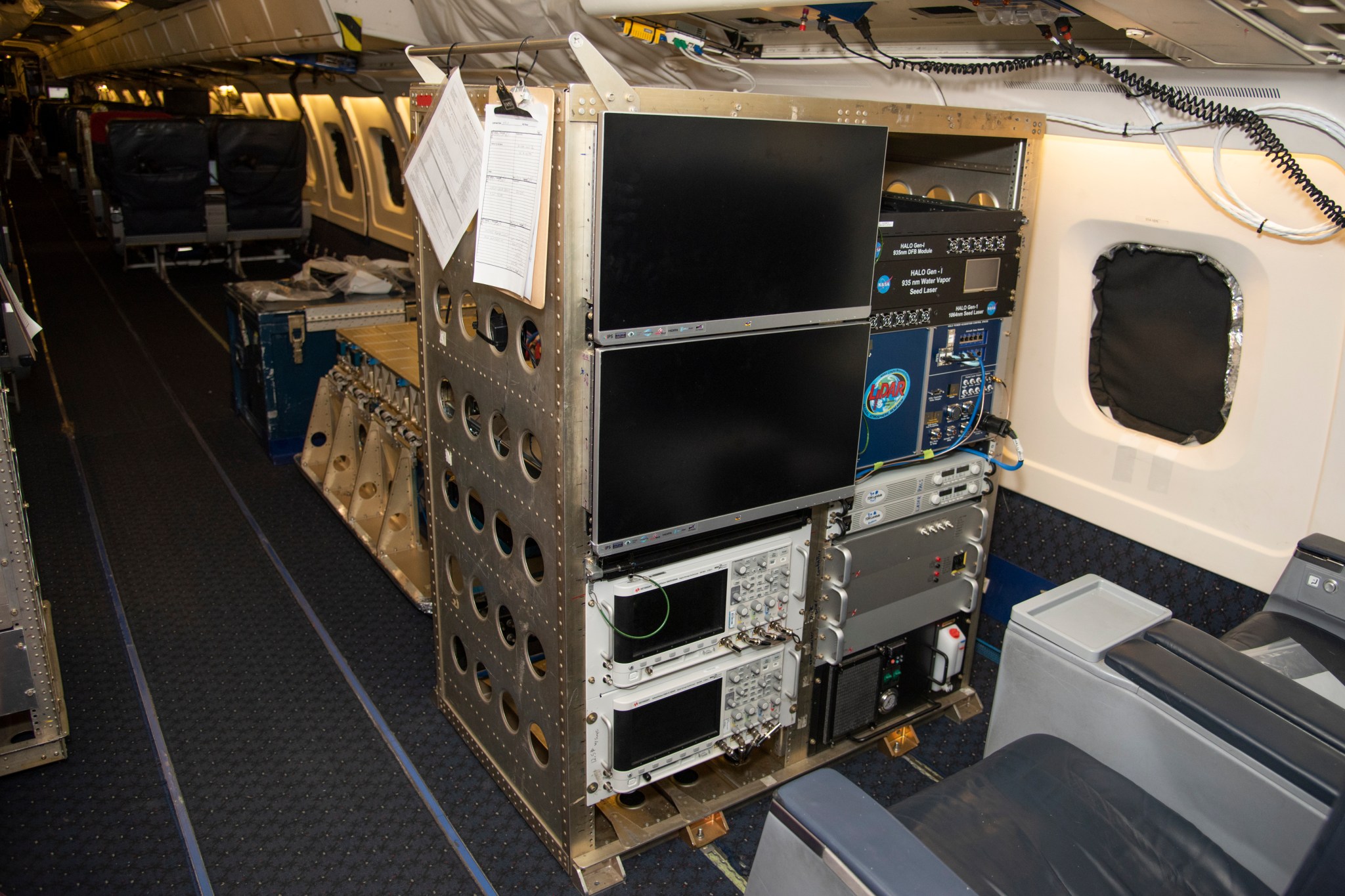 The High Altitude Lidar Observatory (HALO), which has a metal frame housing two computer monitors and other electronic equipment. The whole frame is bolted to the floor of a research plane.