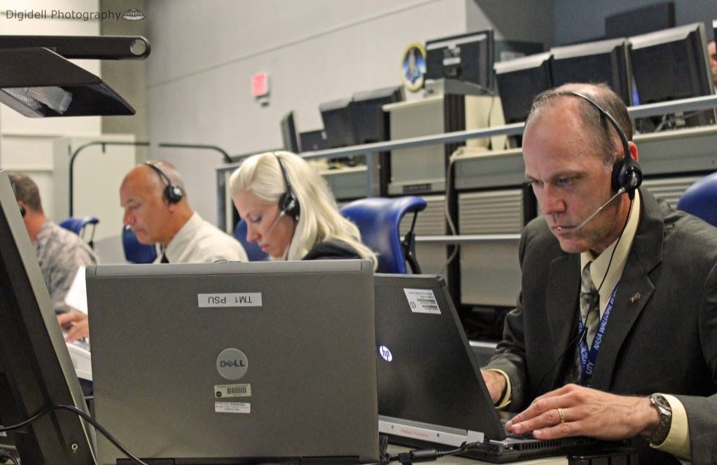 One woman and four men sit looking at computers side by side in the range control center