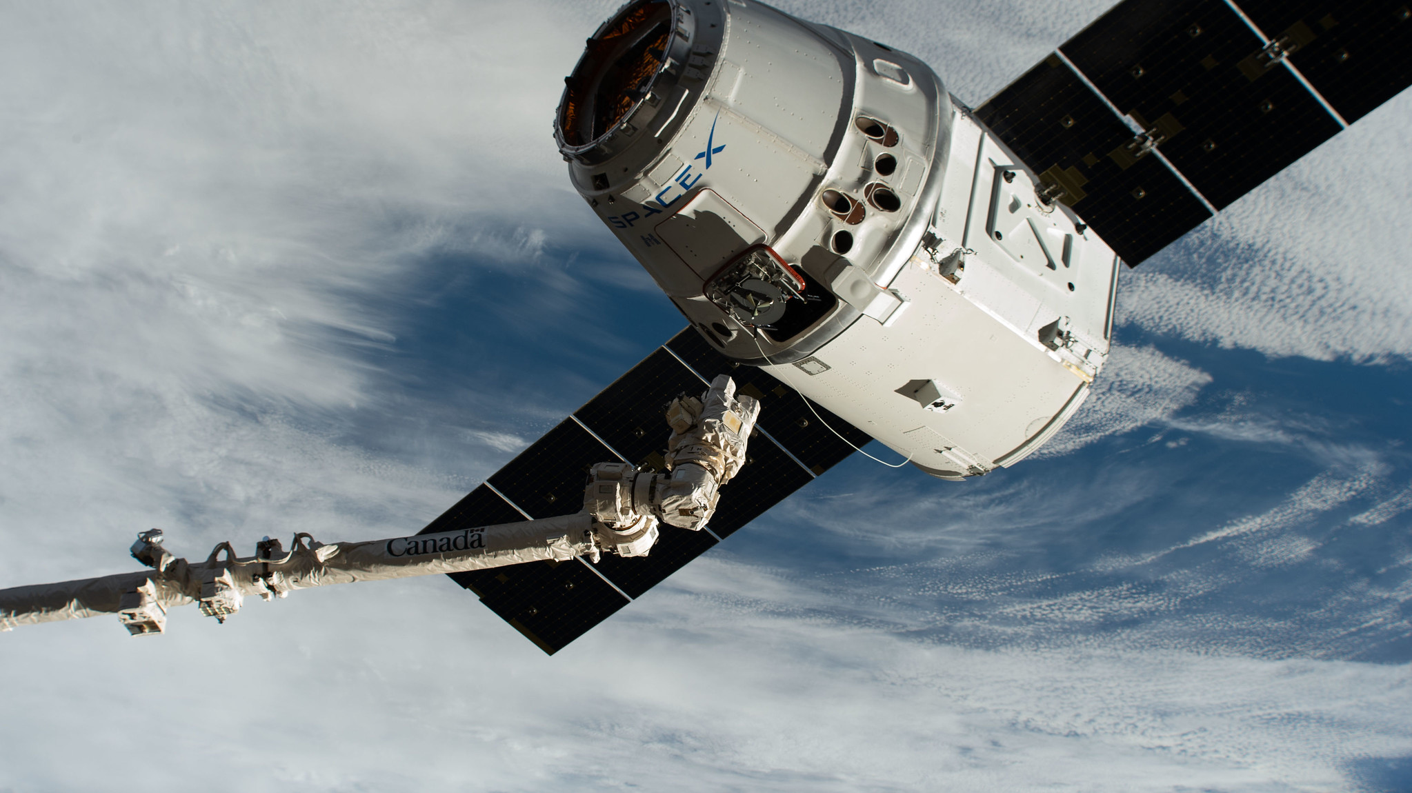 The Canadarm2 robotic arm, commanded by astronaut David Saint-Jacques, reaches out to grapple the SpaceX Dragon cargo craft