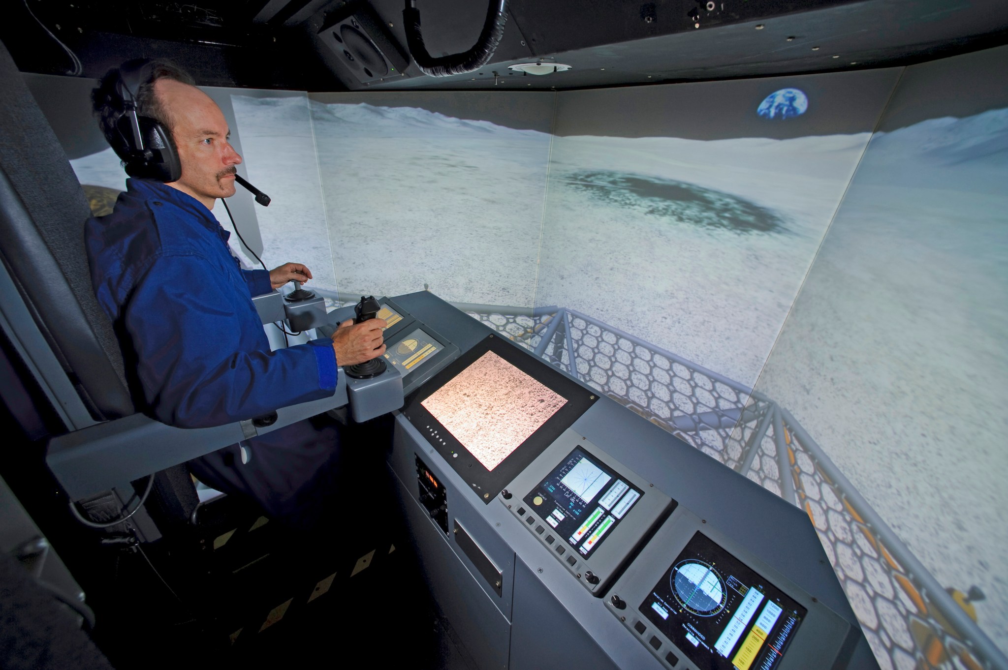 A pilot stands at the controls of the VMS and views the out-the-window displays of the lunar surface.