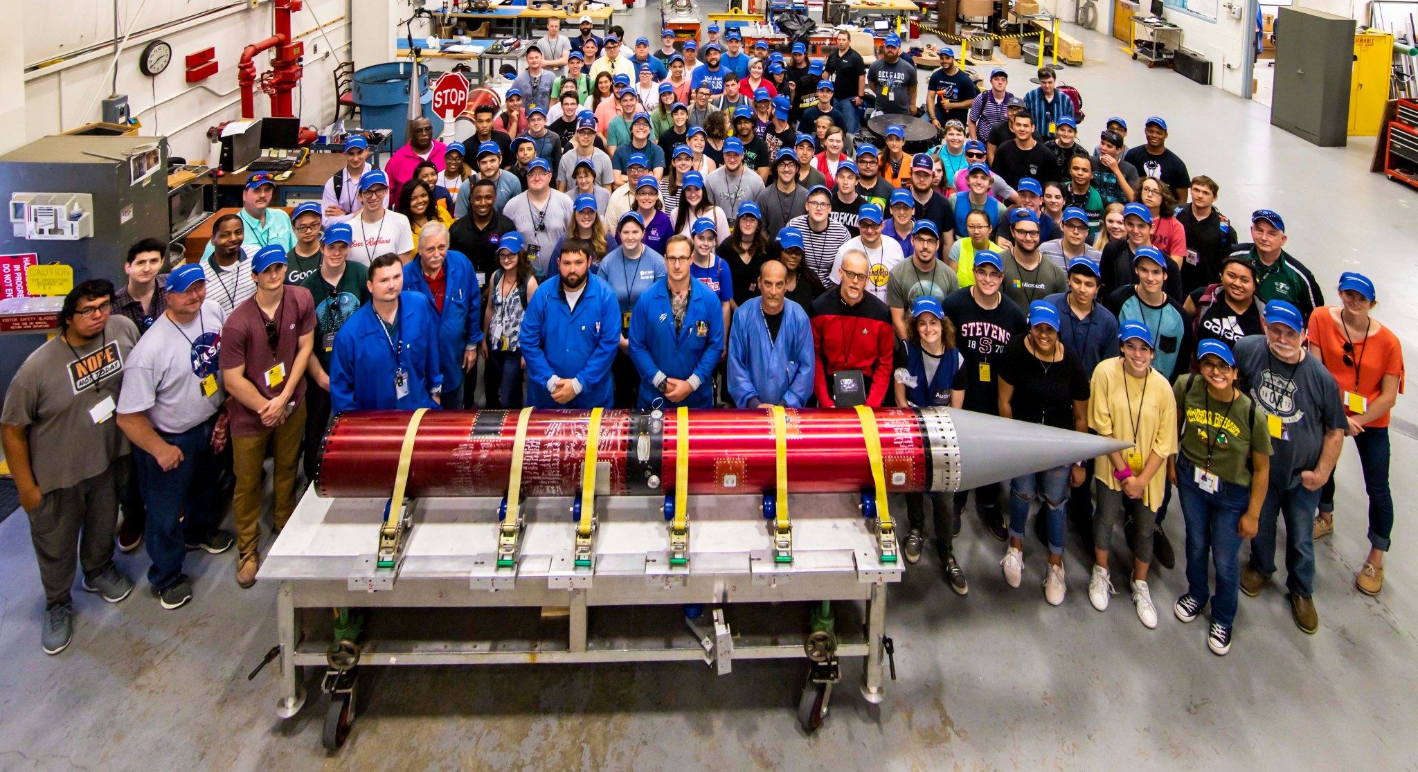 A large group of people poses for a group photo behind their sounding rocket payload.