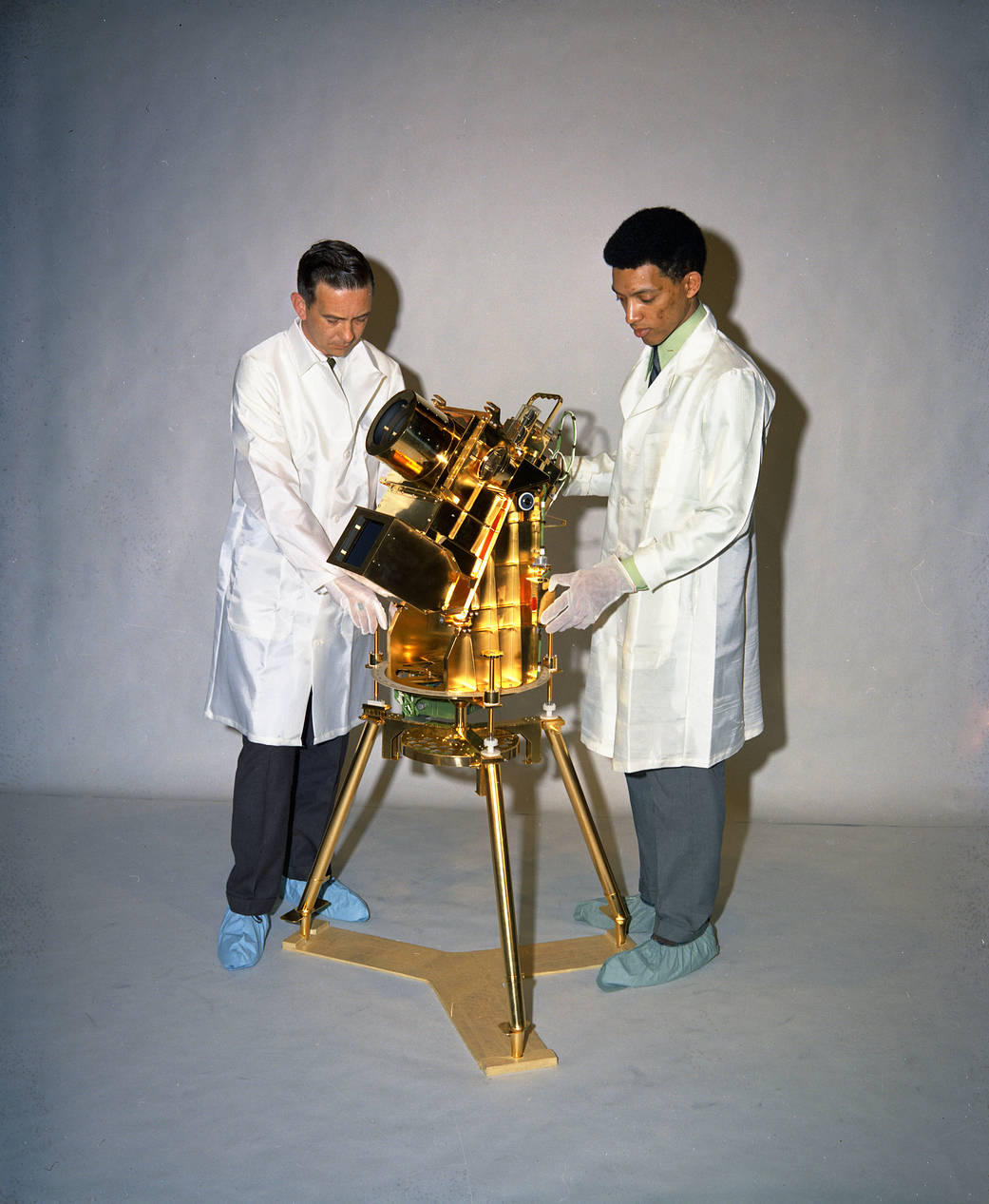Two men stand on either side of a gold camera, which stands about three-quarters of their height. 