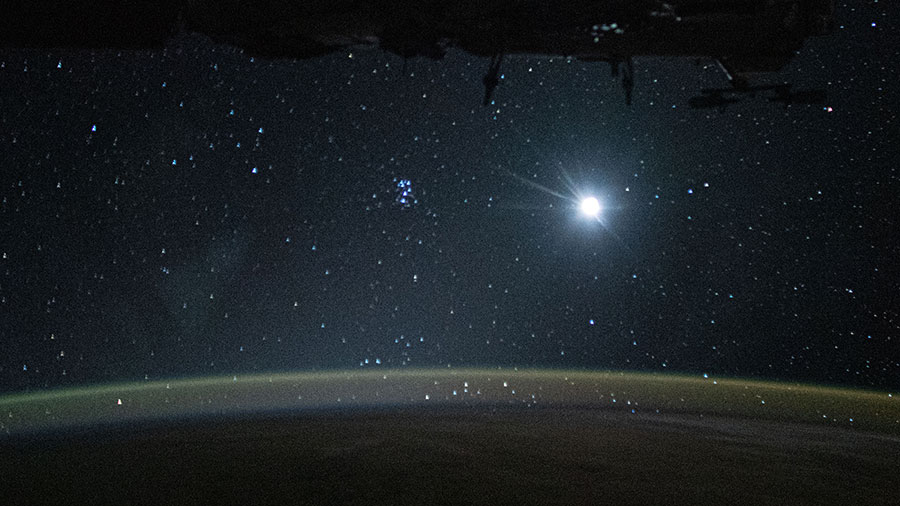 Earth's atmospheric glow, highlighted by the Moon and a starry orbital nighttime