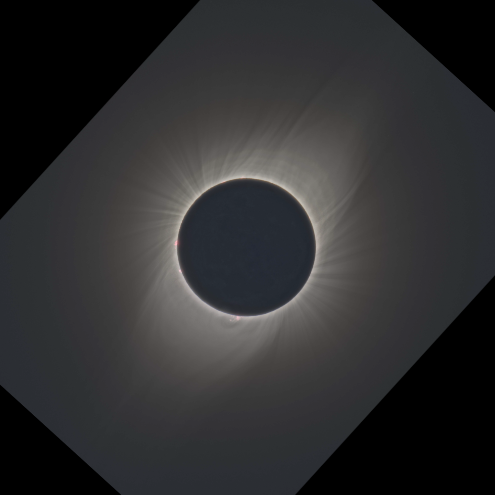 A photo of a total solar eclipse on July 2, 2019, taken from Chile. The Sun is completely covered by the Moon, and together they appear like a dark gray circle in the center of the image with a white outline and delicate, wispy white rays of light extending out from behind the circle. The rest of the sky is dark gray. Because the image was taken at an angle, it only covers a diamond-shaped part of the center, with black background making up the rest of the square.