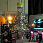 A laboratory showing equipment from the In situ Carbon Evolution Experiments (ICEE) chamber. Bright yellow flask and a glowing substance coming from one tube featuring high power pressure valves that have bright pink colors coming from the tubing.