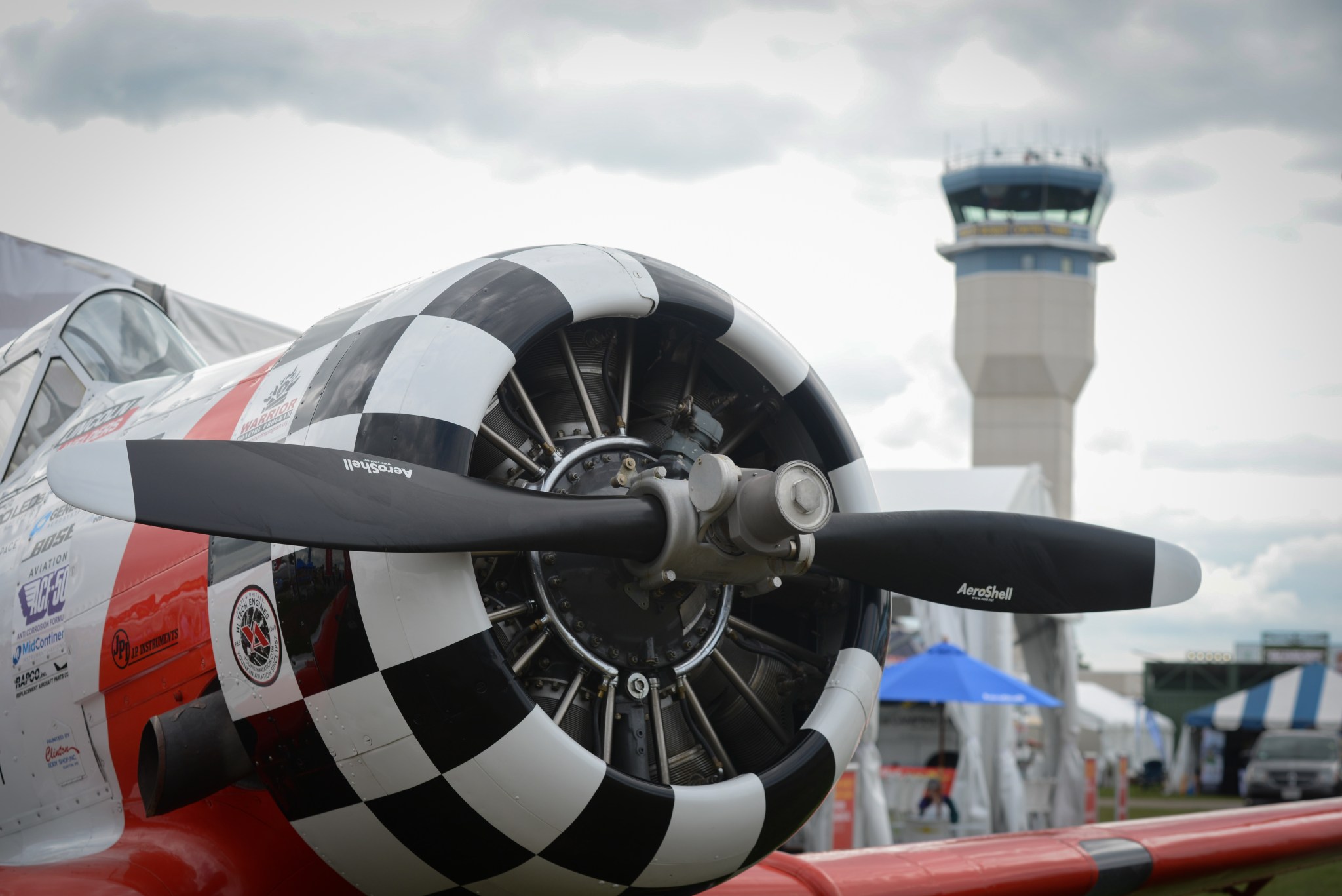 The business end of a North American AT-6 Texan aircraft sits with the Oshkosh air traffic control tower in the background.
