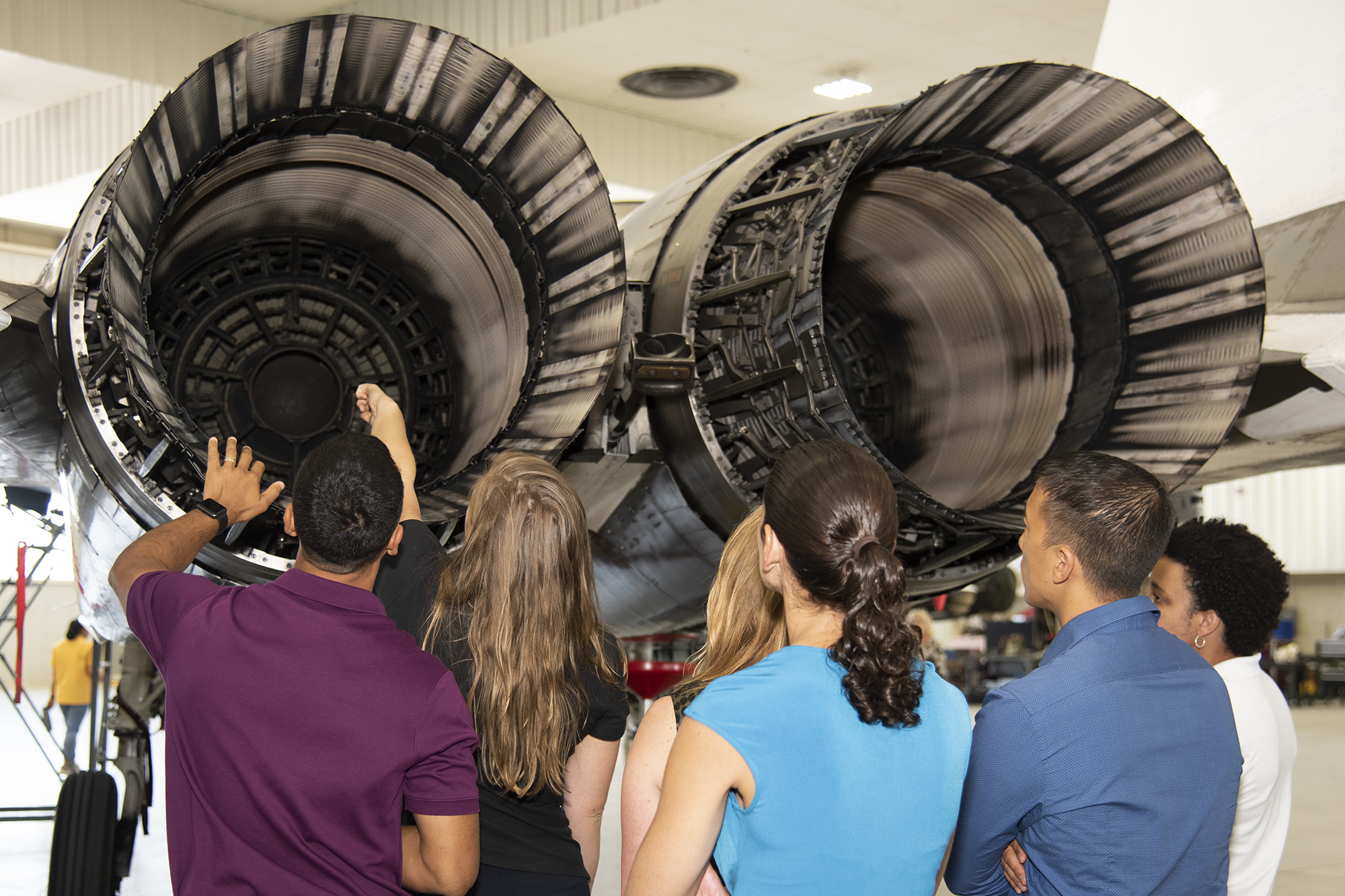 NASA's 2017 astronaut candidates look inside the engine nozzle of an F-15 jet.