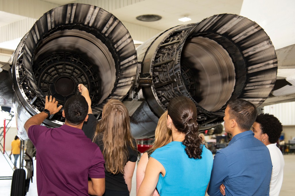 NASA's 2017 astronaut candidates look inside the engine nozzle of an F-15 jet.