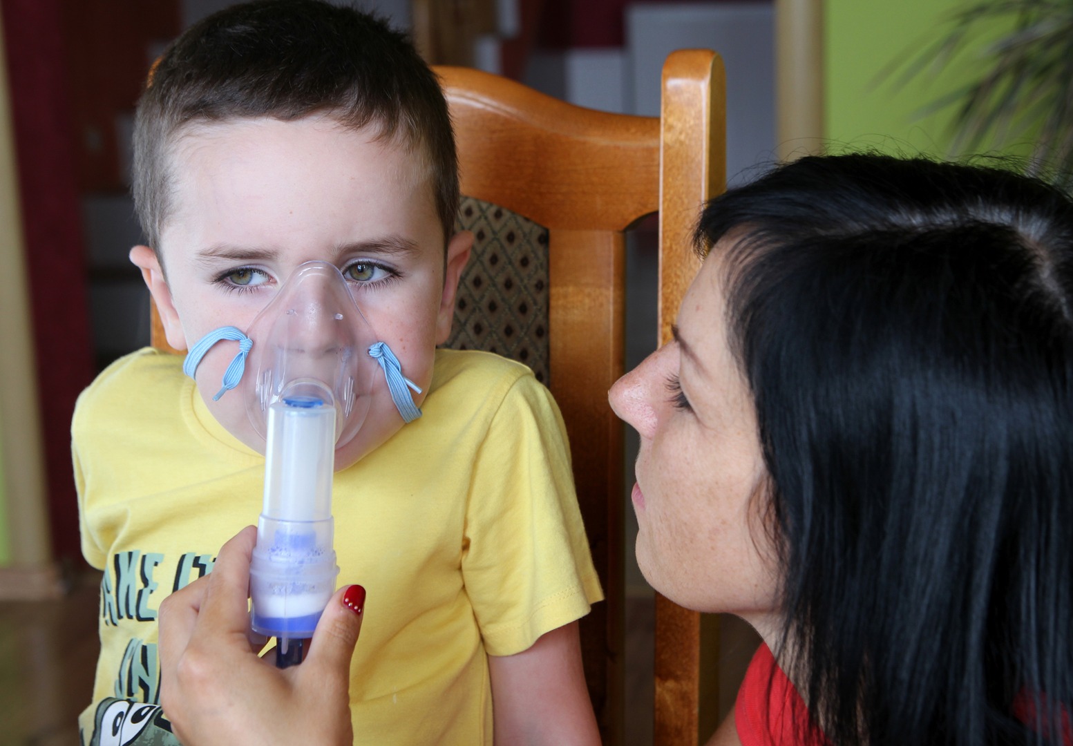 A child with a nebulizer mask over their face, held up by their parent.