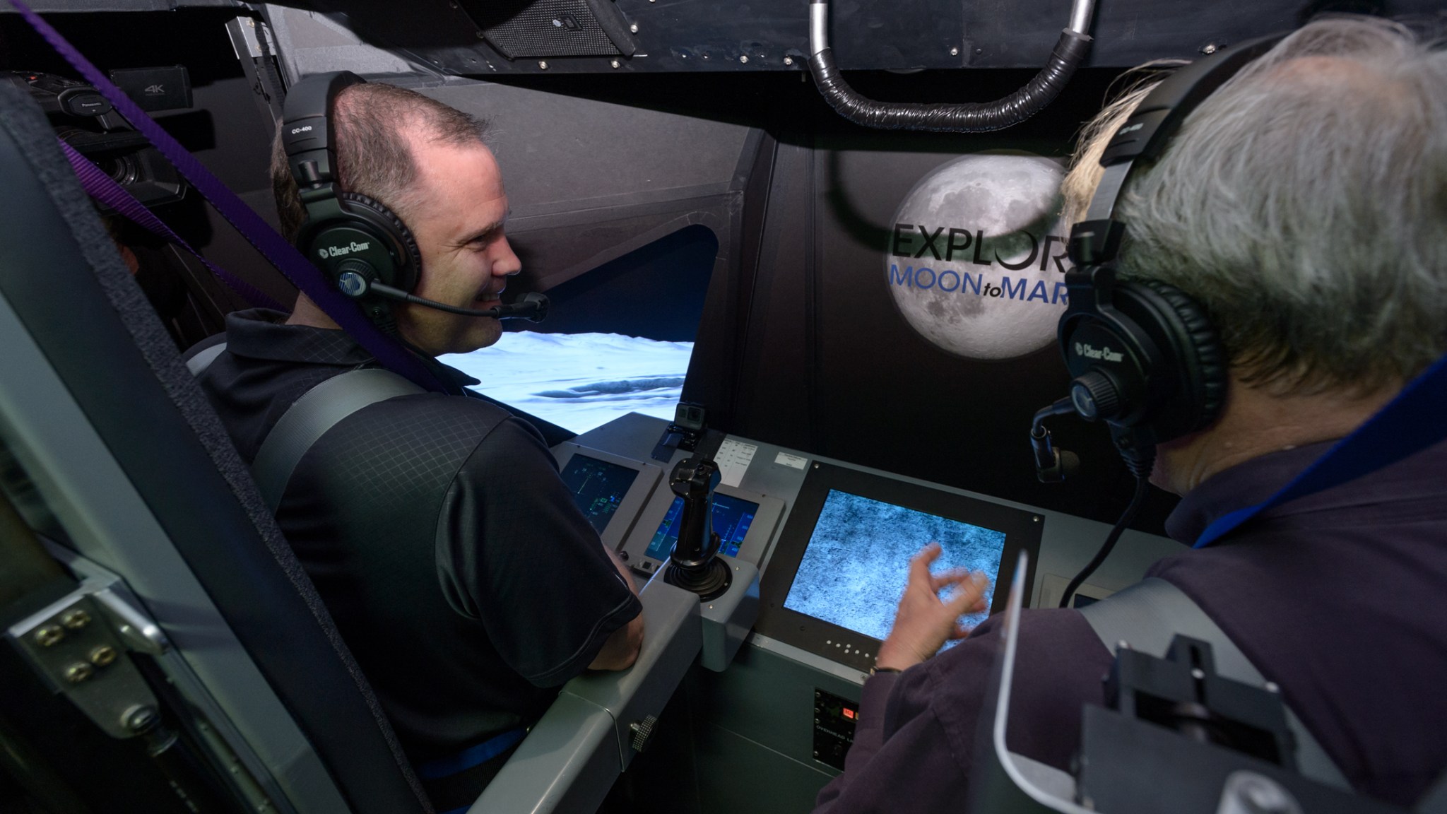 NASA Administrator Jim Bridenstine wearing a headset stands at the controls in a cockpit mocked up like the Apollo Lunar Module.