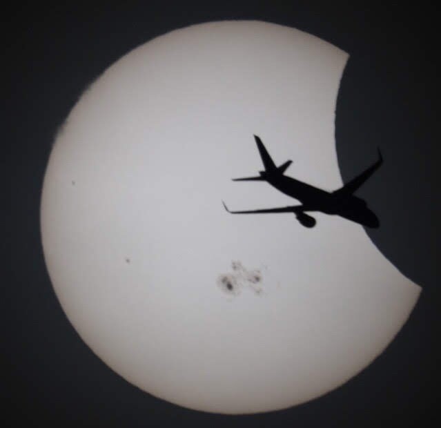 A photograph through a telescope of an airplane silhouetted against a partial solar eclipse.