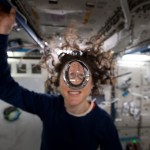 Astronaut on the International Space Station smiles behind a floating bubble of water. 
