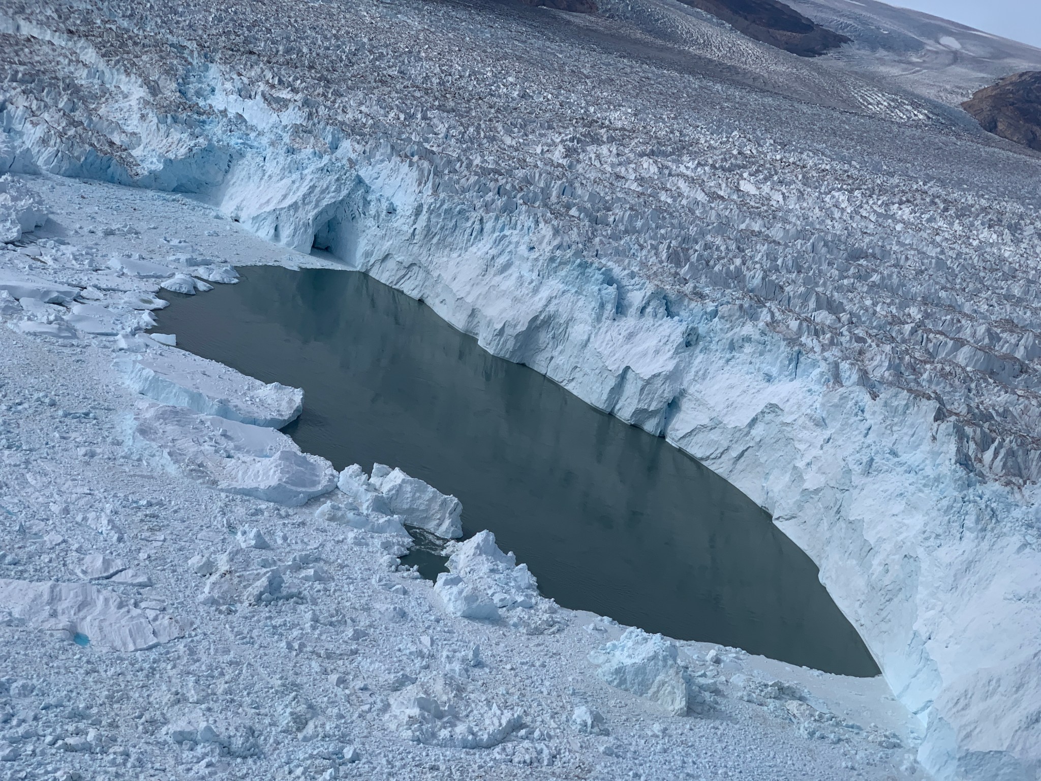 A hole in sea ice where the ocean water peeks through. The ice is chunky and almost blue with a smooth pool of water.