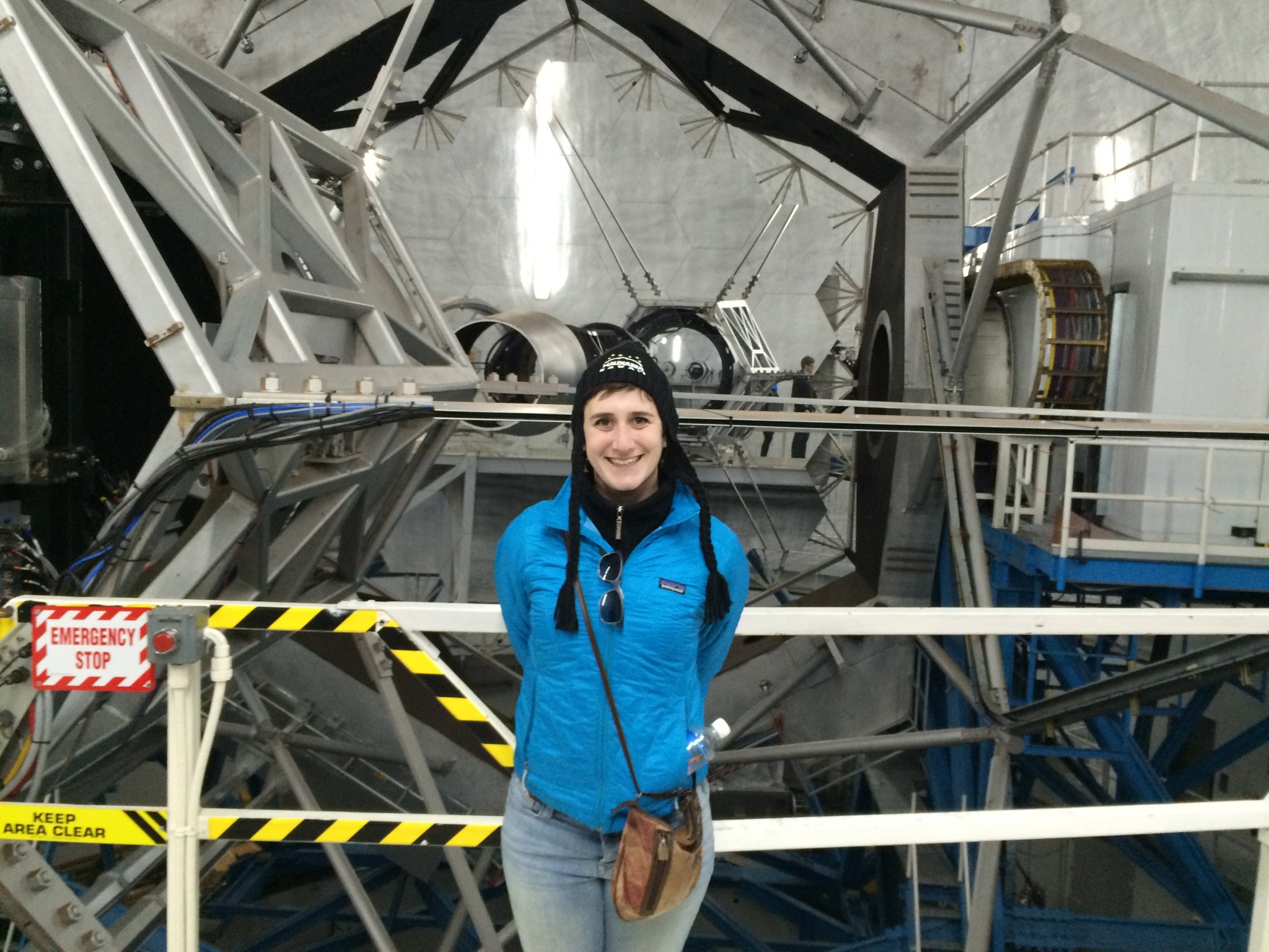 astronomer Lauren Weiss wears a blue jacket and a hat and stands in front of a large telescope