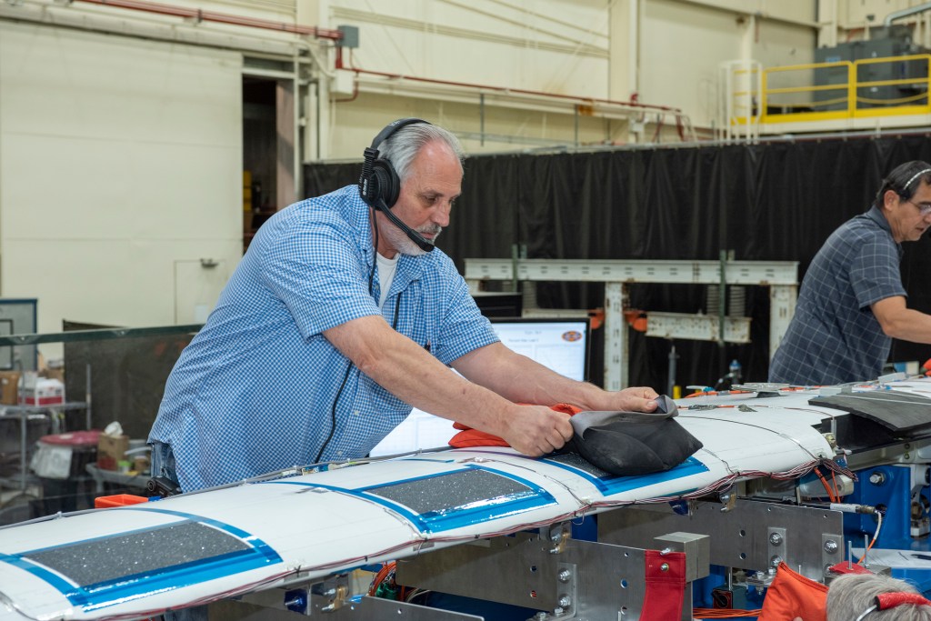 Technicians apply shot bags to the wing of the X-57 distributed electric aircraft wing.