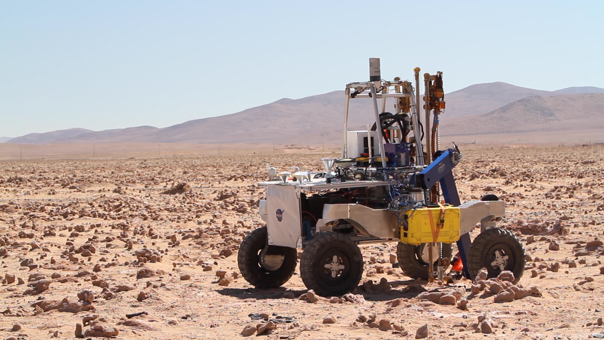 A four-wheeled rover in a dramatic desert landscape with instrumentation and a drill mounted on top of it.