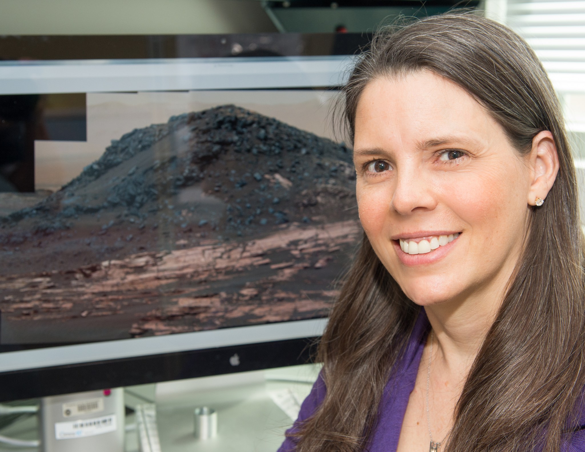 A woman smiles in front of a photo of Mars. 